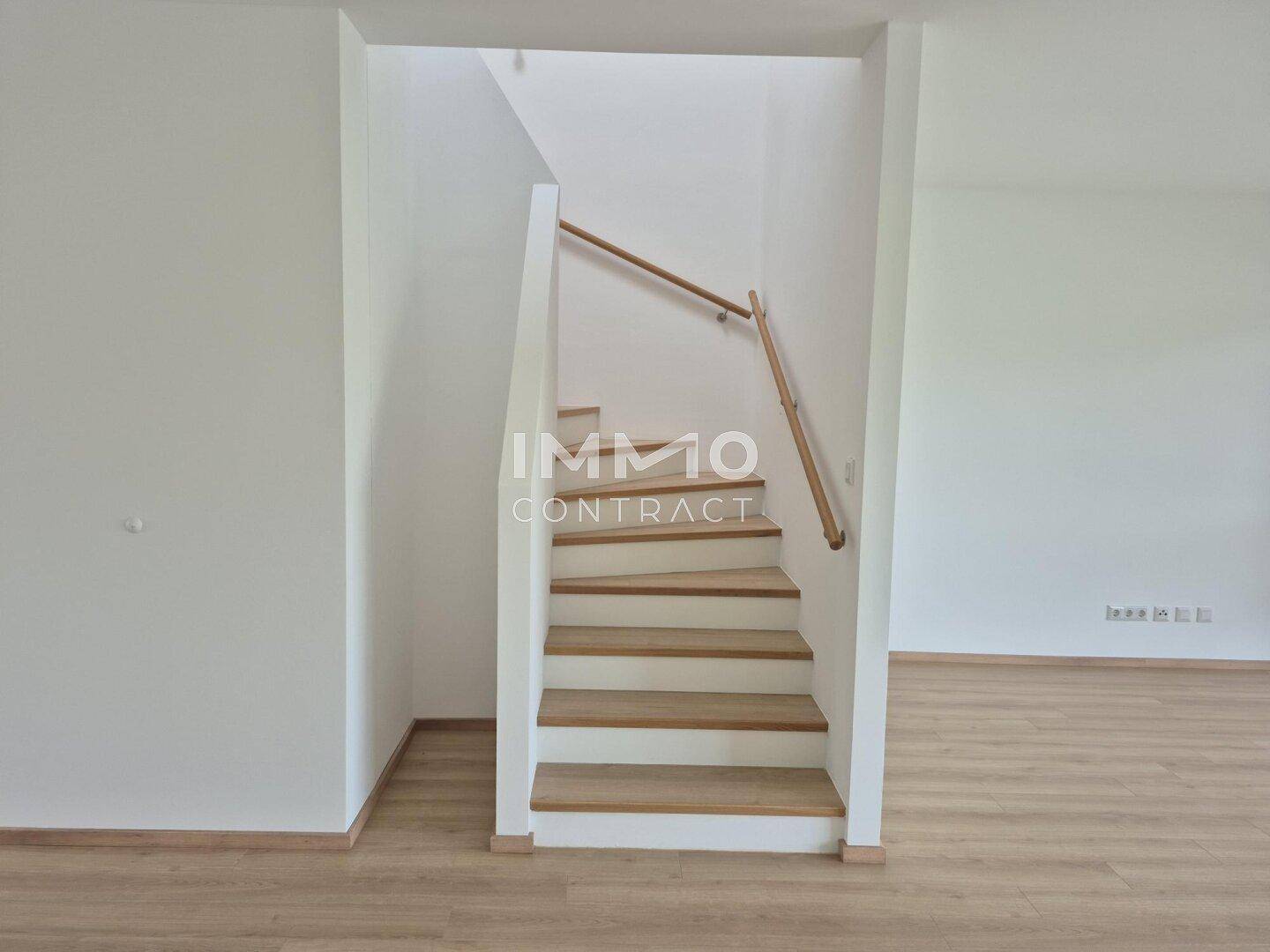 Moderne Holztreppe mit weißem Geländer, die die verschiedenen Etagen des Hauses stilvoll verbindet.