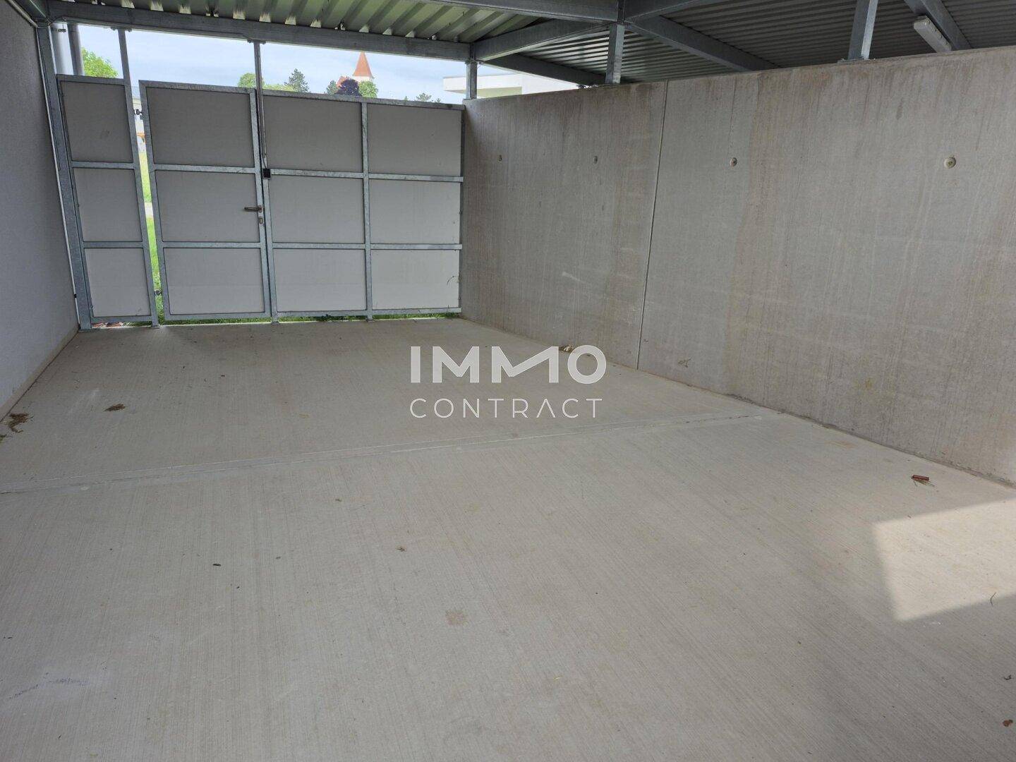 Geräumiger überdachter Abstellbereich im Freien mit Betonboden und Metalltor.