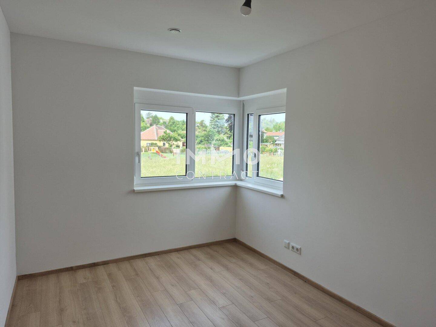 Helles Schlafzimmer mit Laminatboden und Eckfenstern mit Blick ins Grüne.