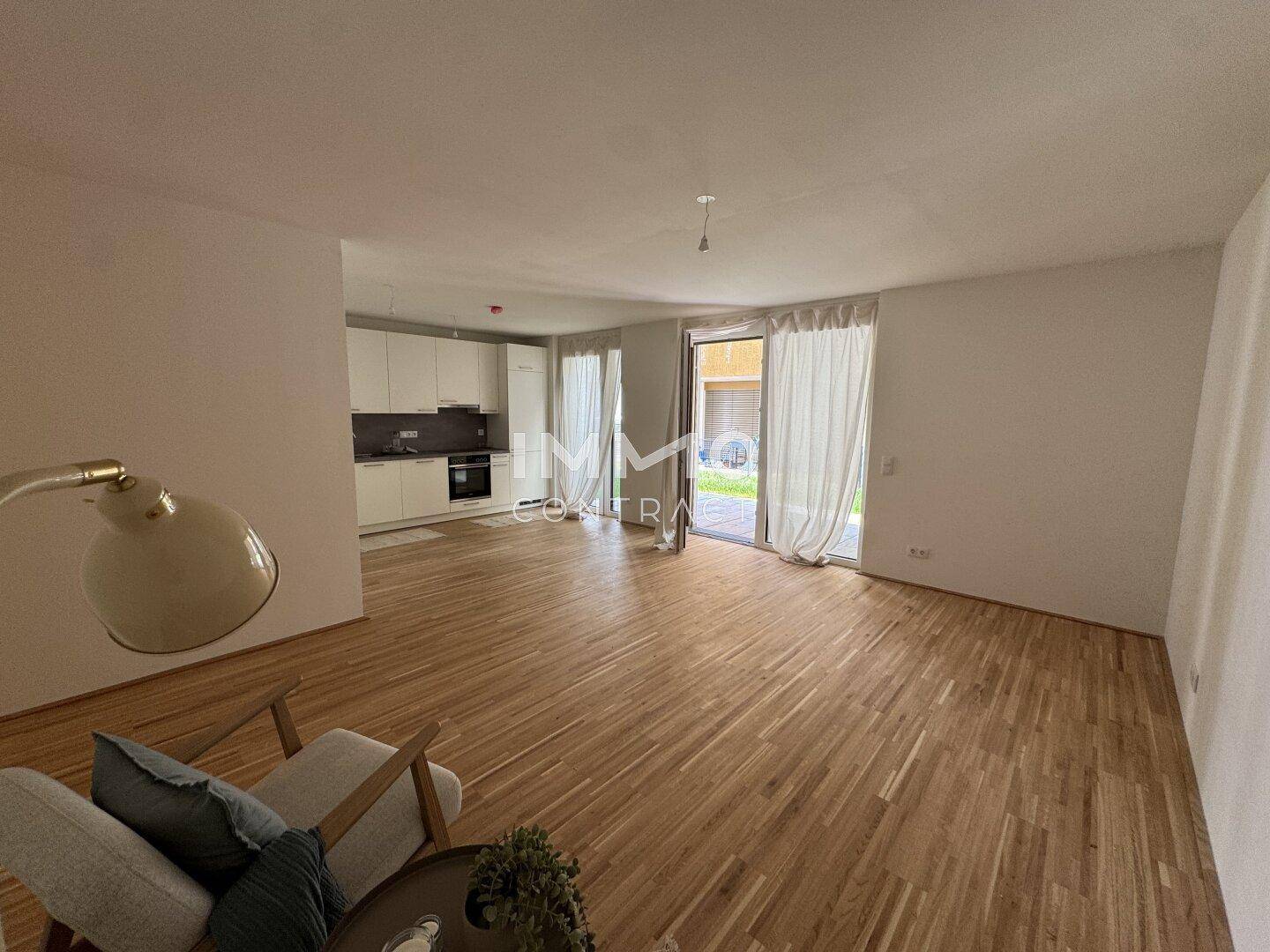 Offener Wohnbereich mit Holzboden, moderner Küche im Hintergrund und Zugang zum Garten.