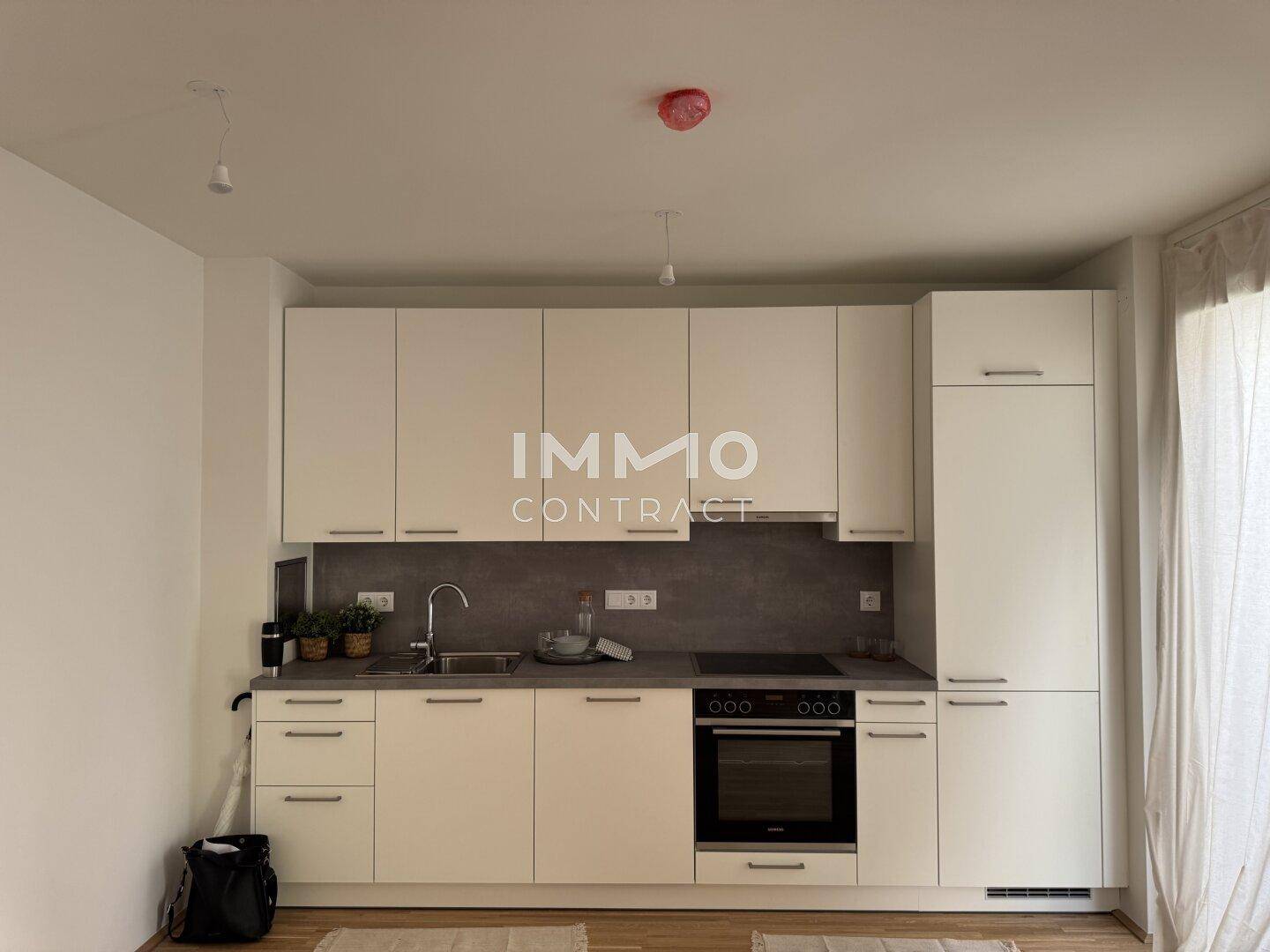 Moderne Einbauküche mit weißen Schränken, grauer Arbeitsplatte und integriertem Backofen.