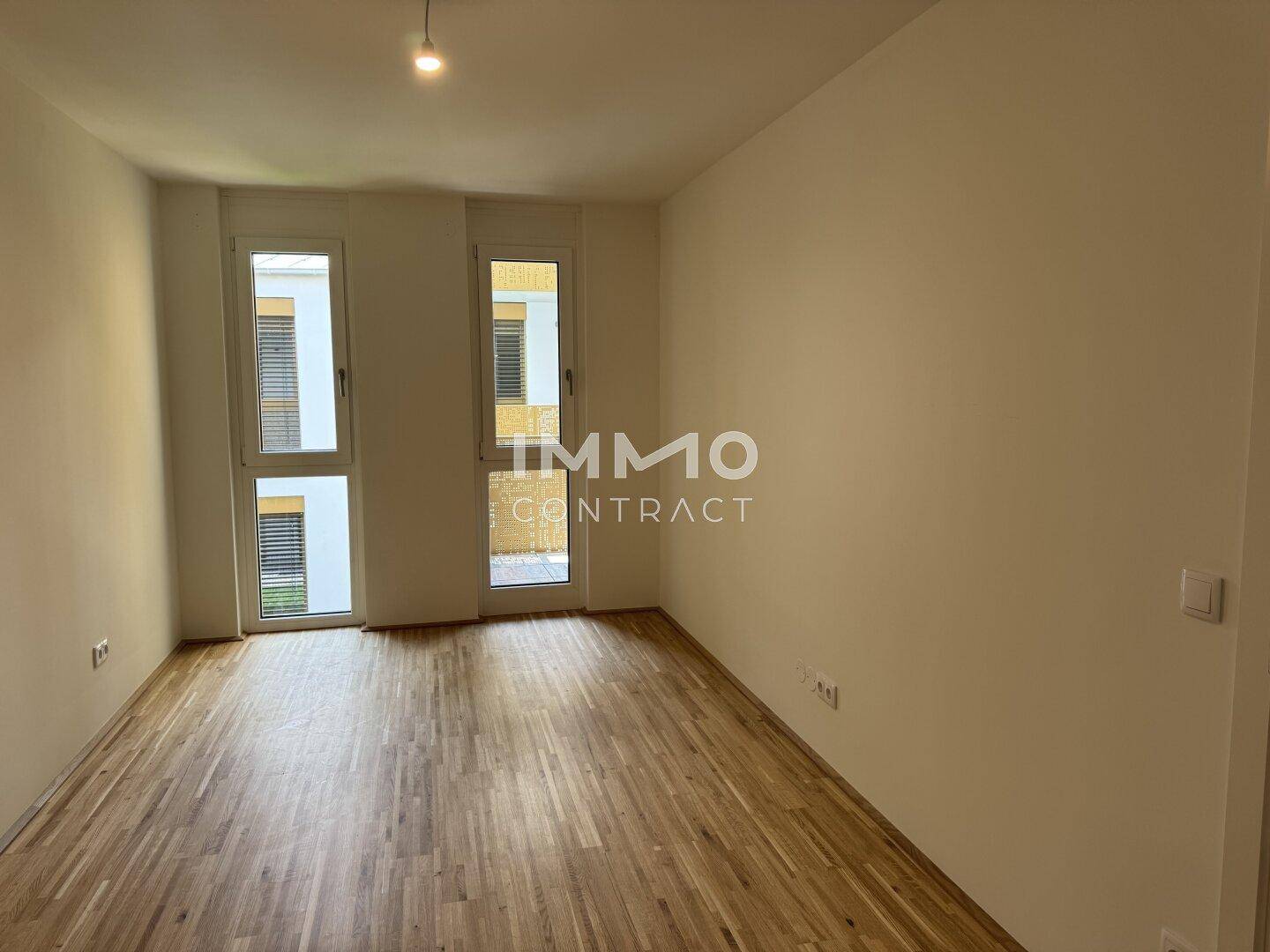 Leeres Zimmer mit Holzparkettboden und großen Fenstern, die viel Tageslicht hereinlassen.