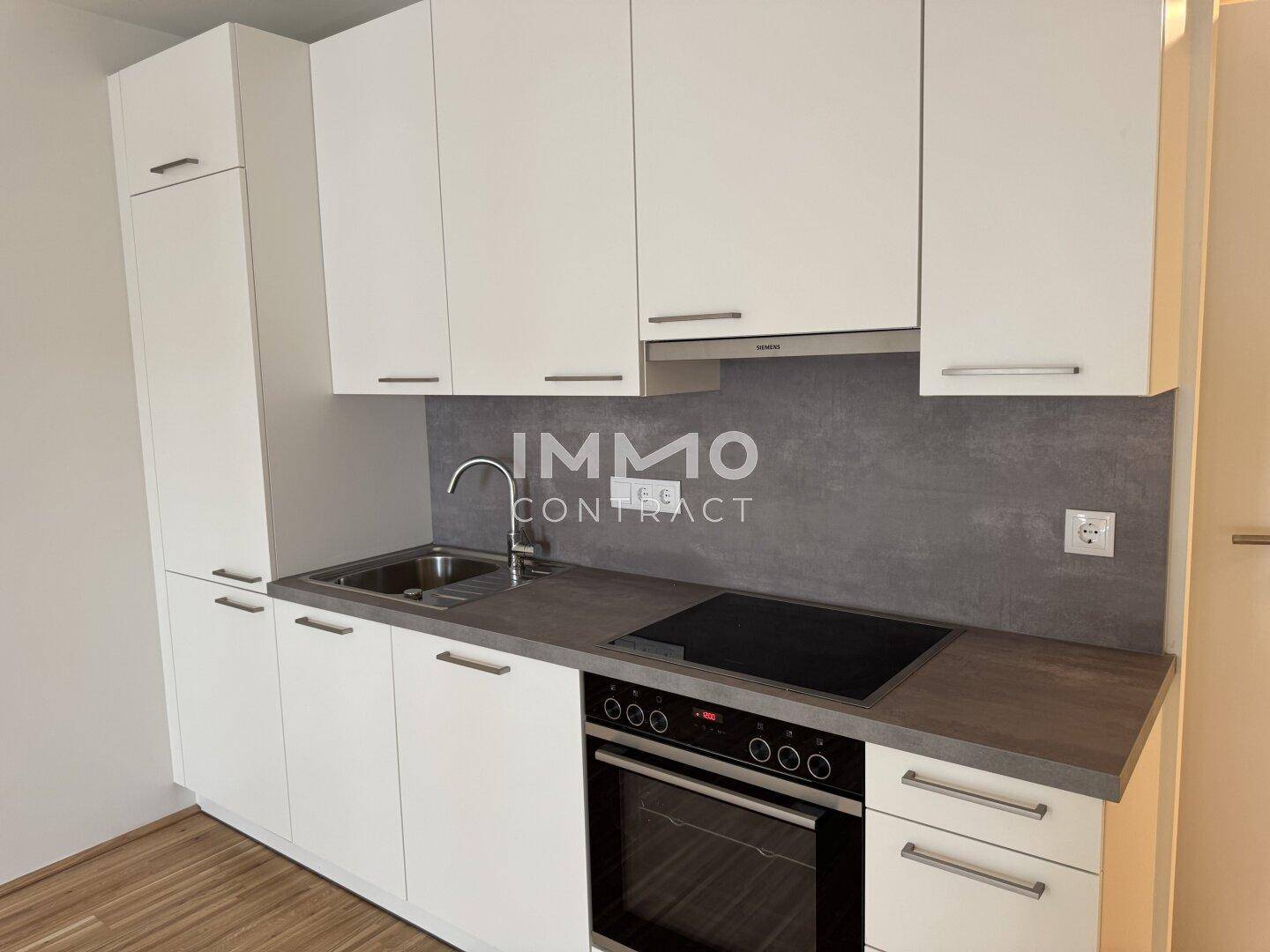 Moderne Einbauküche mit weißen Schränken, dunkler Arbeitsplatte und integrierten Geräten.