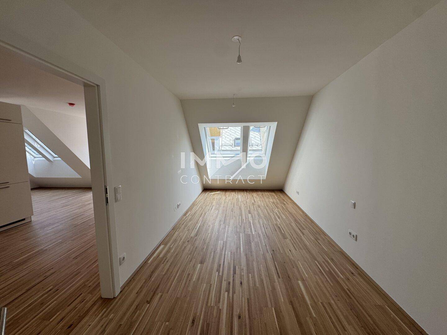 Heller Wohnraum mit Dachschrägen, Parkettboden und großem Dachfenster.