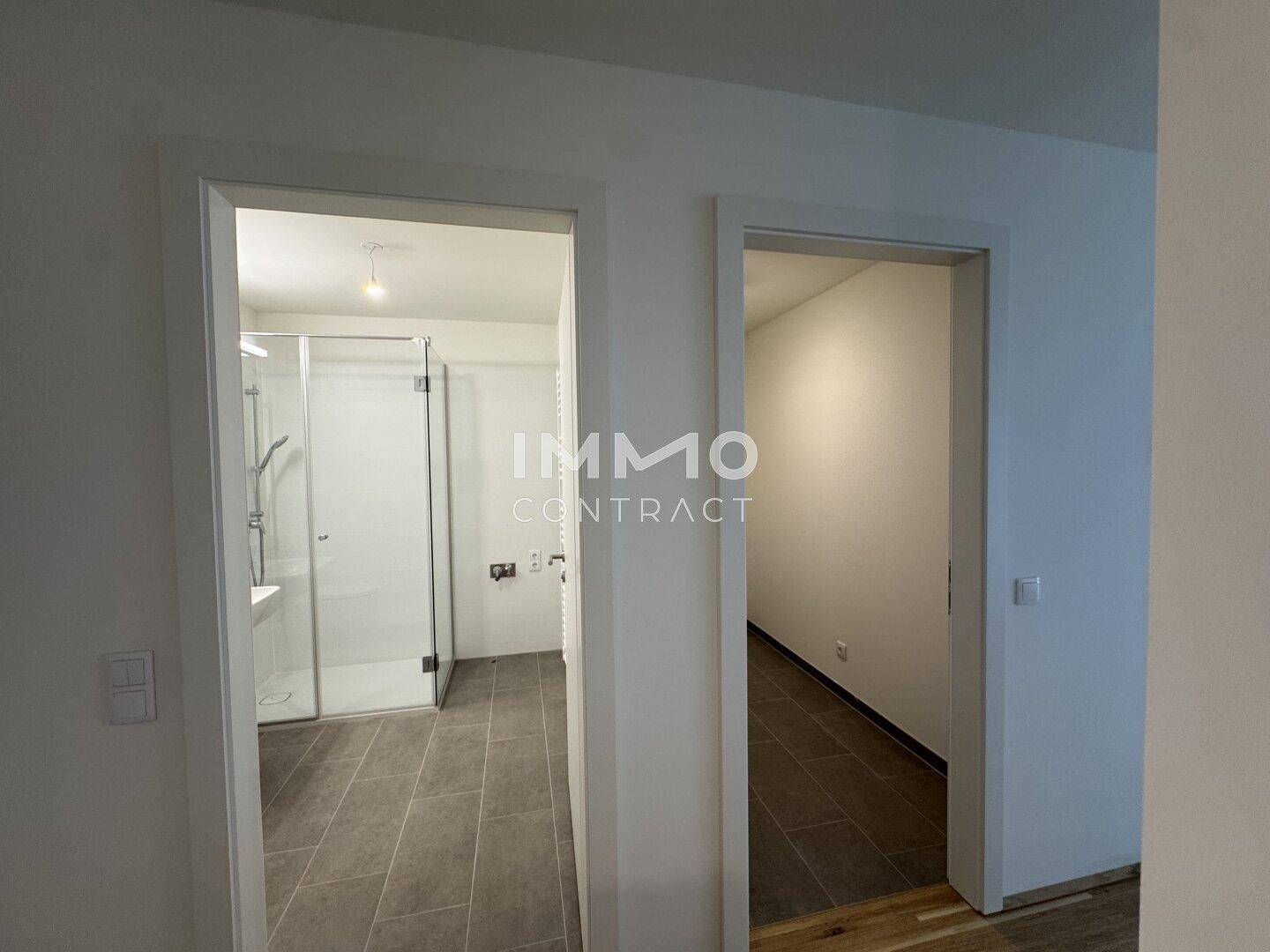 Heller Flur mit Zugang zu einem modernen Badezimmer mit Dusche und einem weiteren Raum.