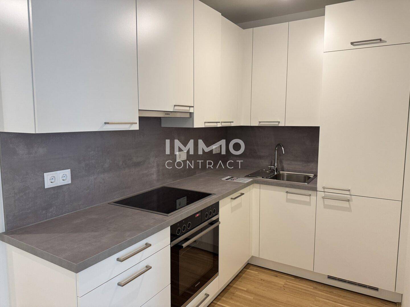 Moderne Einbauküche mit weißen Schränken, grauer Arbeitsplatte und integrierten Geräten.