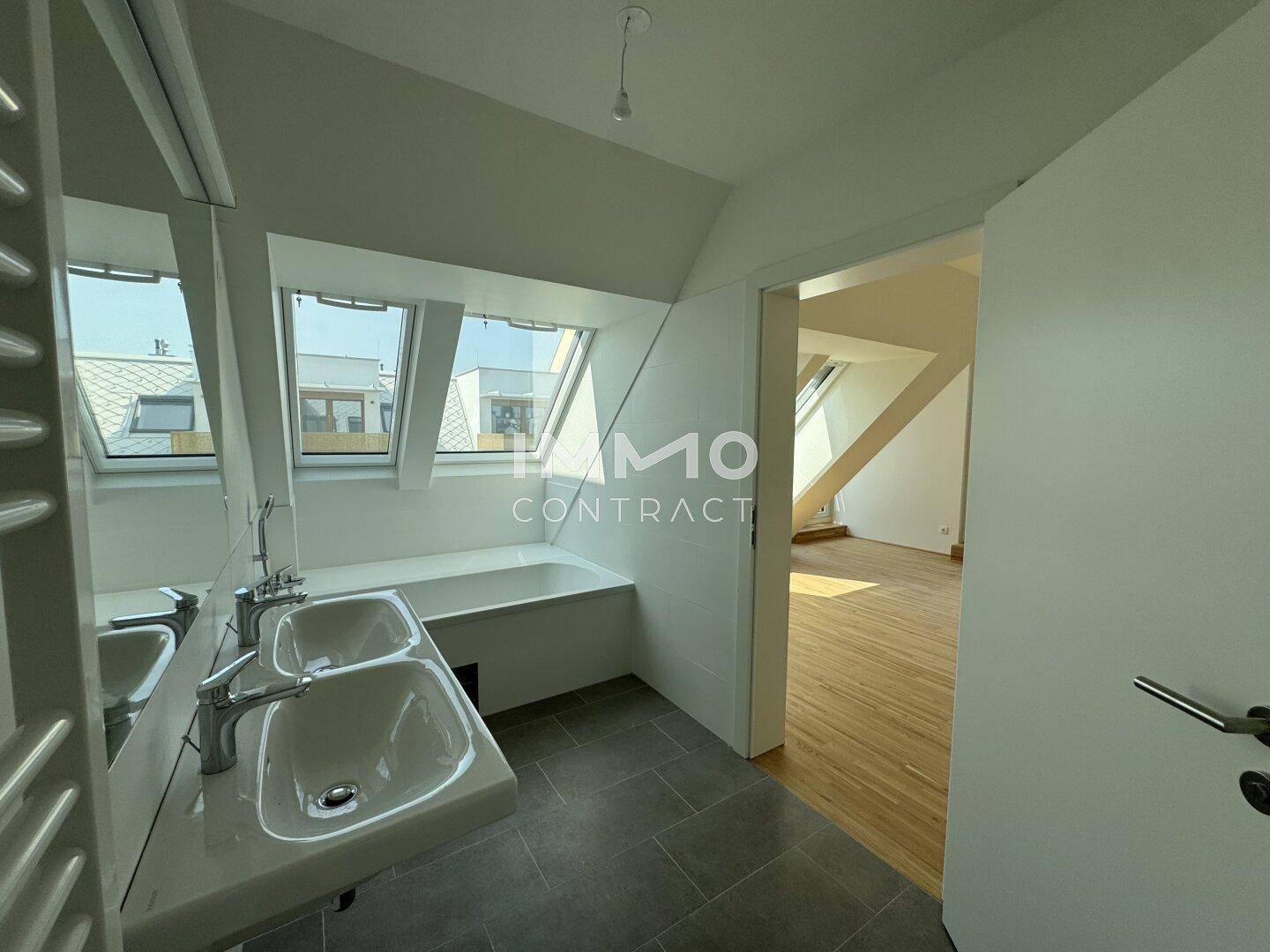 Badezimmer im Dachgeschoss mit Doppelwaschbecken, Badewanne und schrägen Wänden mit Dachfenstern.