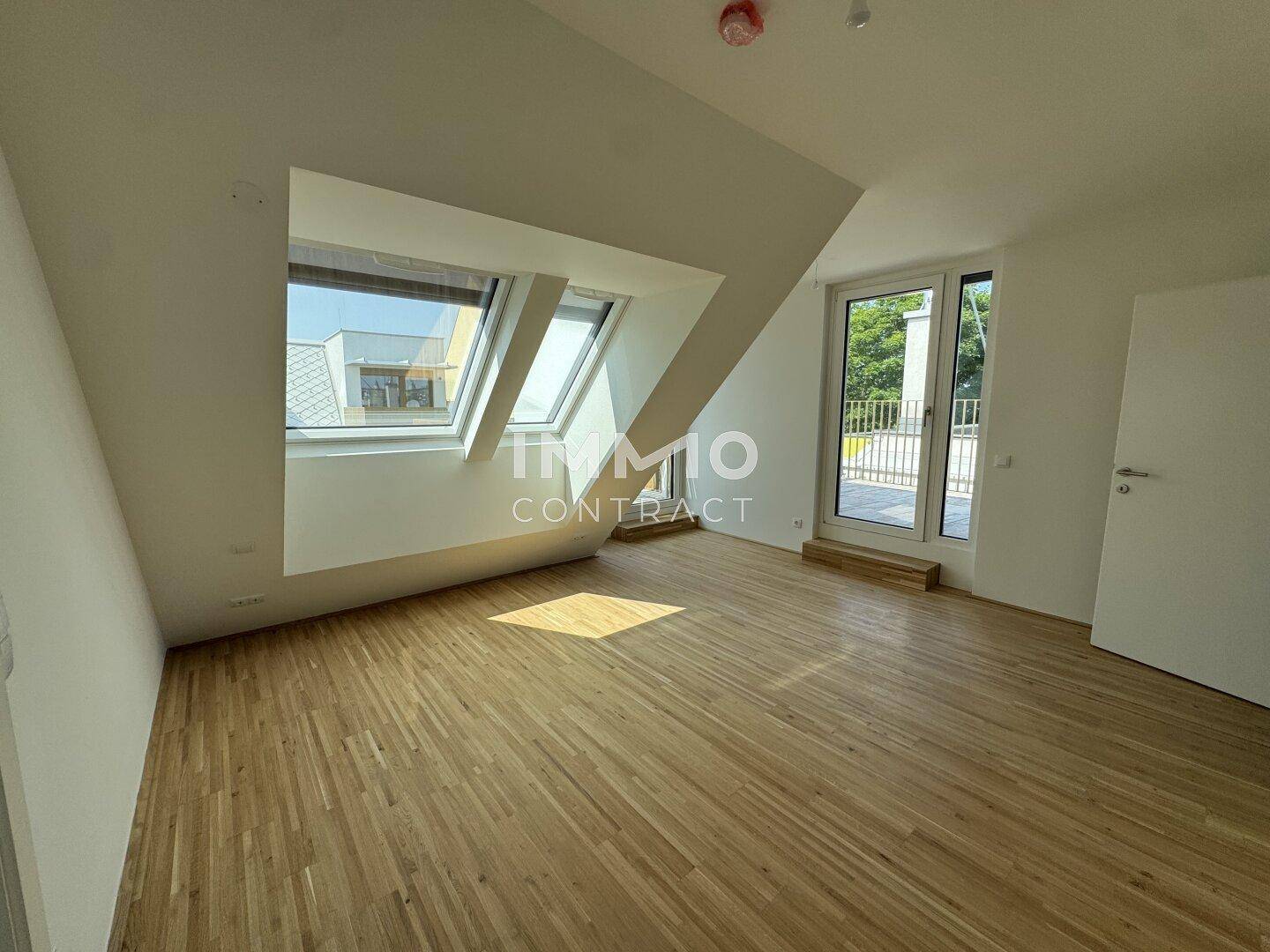 Helles Zimmer im Dachgeschoss mit Holzboden, großen Dachfenstern und Zugang zu einem Balkon.