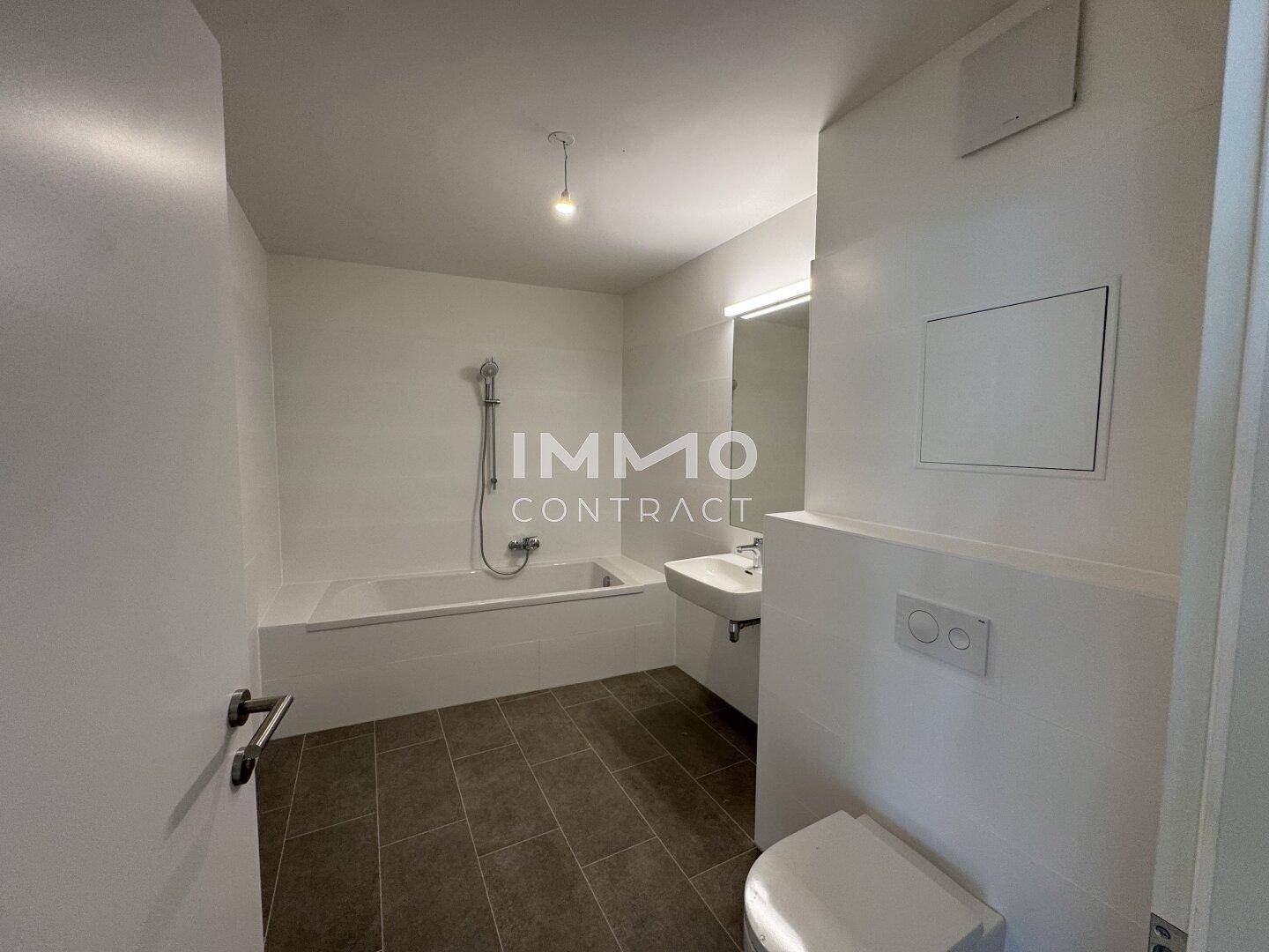 Modernes Badezimmer mit Badewanne, integrierter Dusche, WC und dunklen Bodenfliesen.