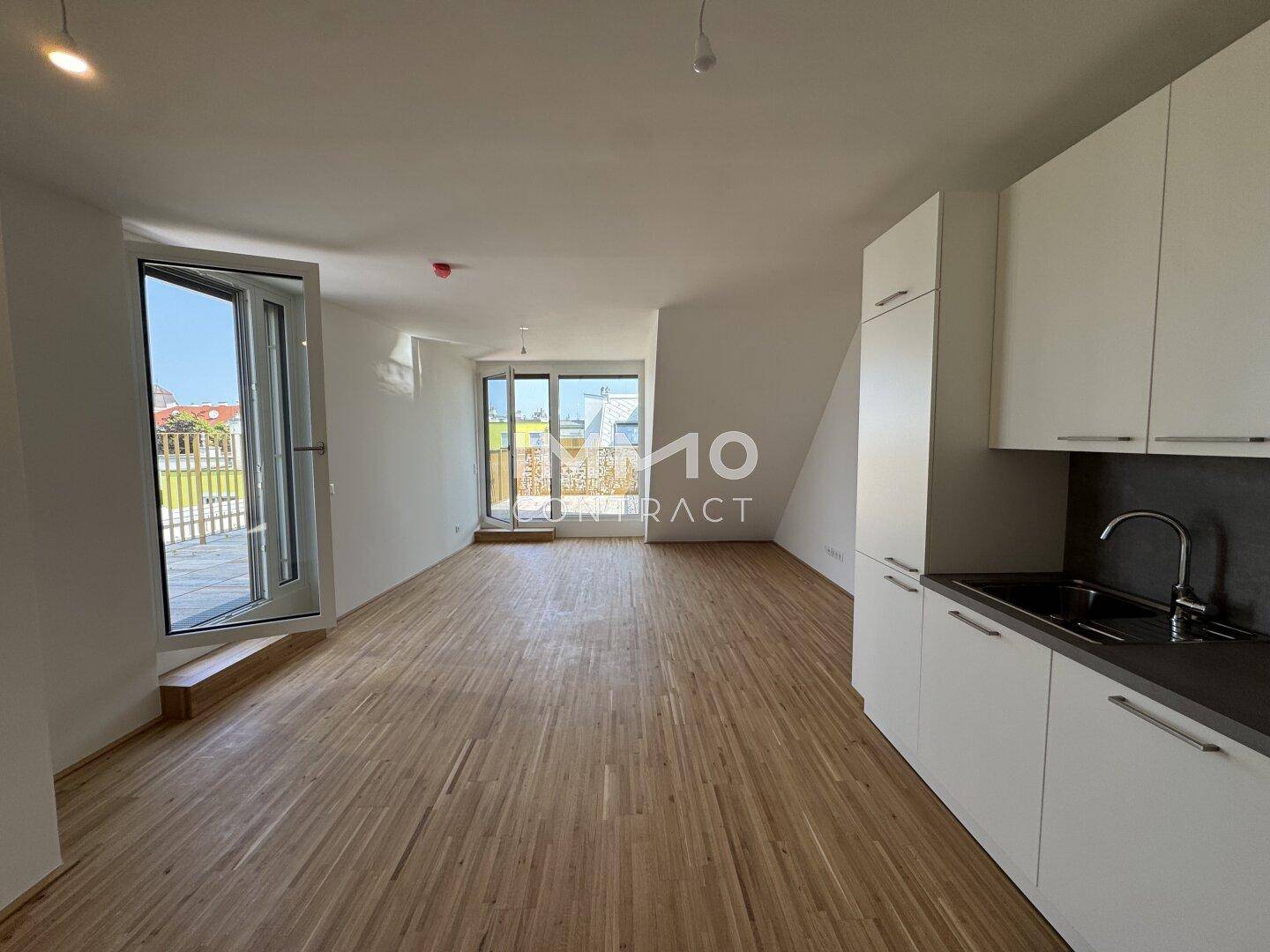 Geräumiger Wohnbereich mit moderner Küchenzeile, Holzboden und großen Fenstern zum Terrassenzugang.