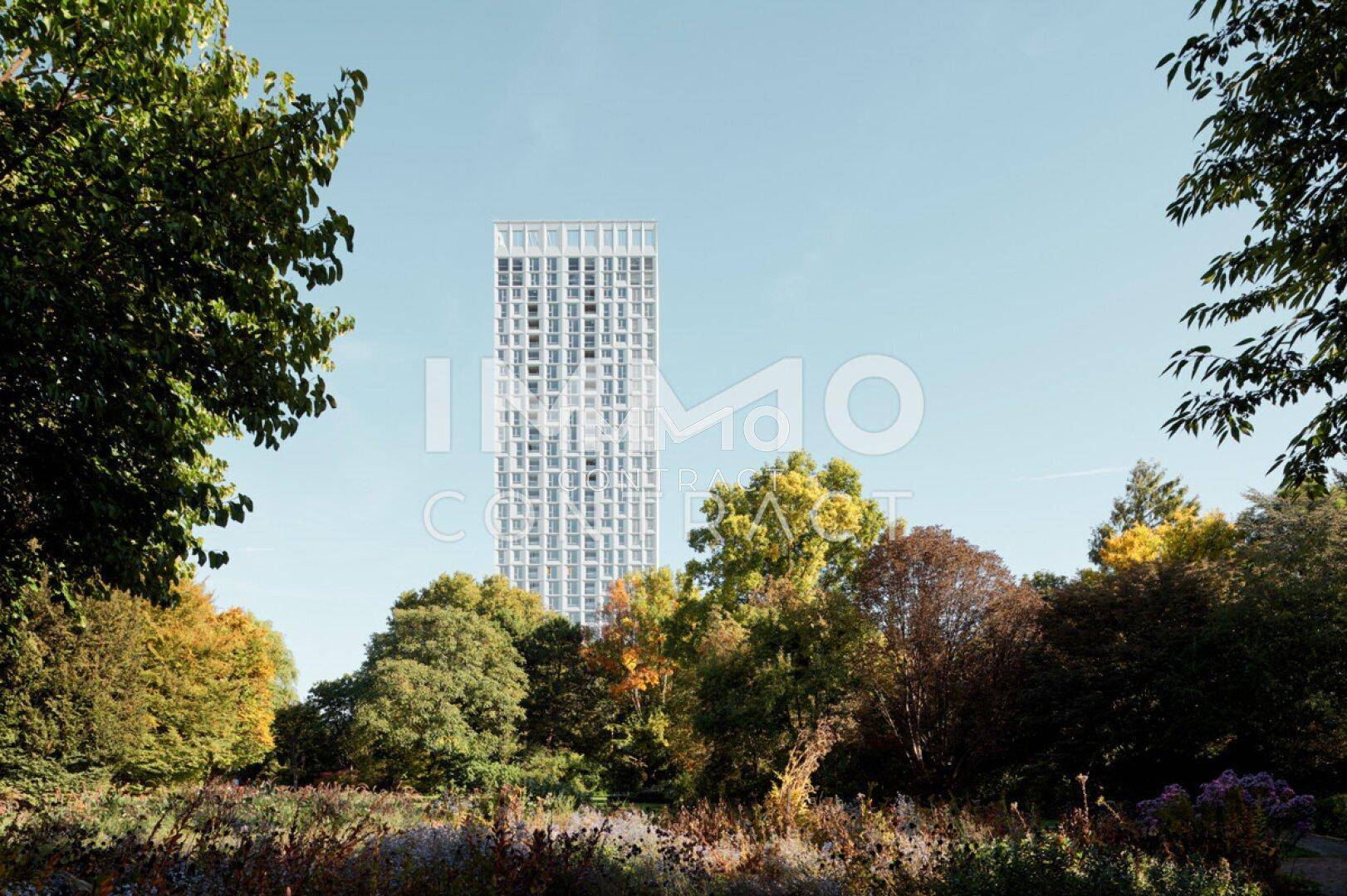 Hohes Wohngebäude inmitten einer grünen Parklandschaft mit Herbstbäumen.