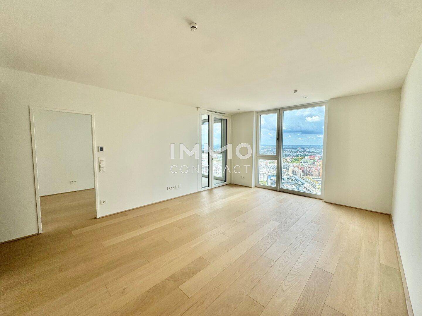 Geräumiges, helles Wohnzimmer mit Holzboden und Panoramafenstern, die einen weiten Stadtblick bieten.