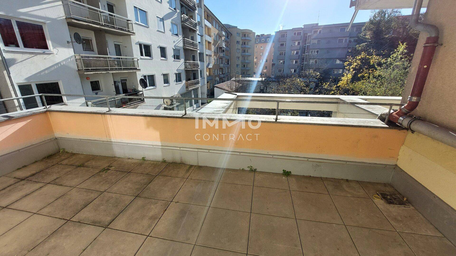 Geflieste Terrasse mit Blick auf umliegende Wohngebäude und viel Sonnenlicht.