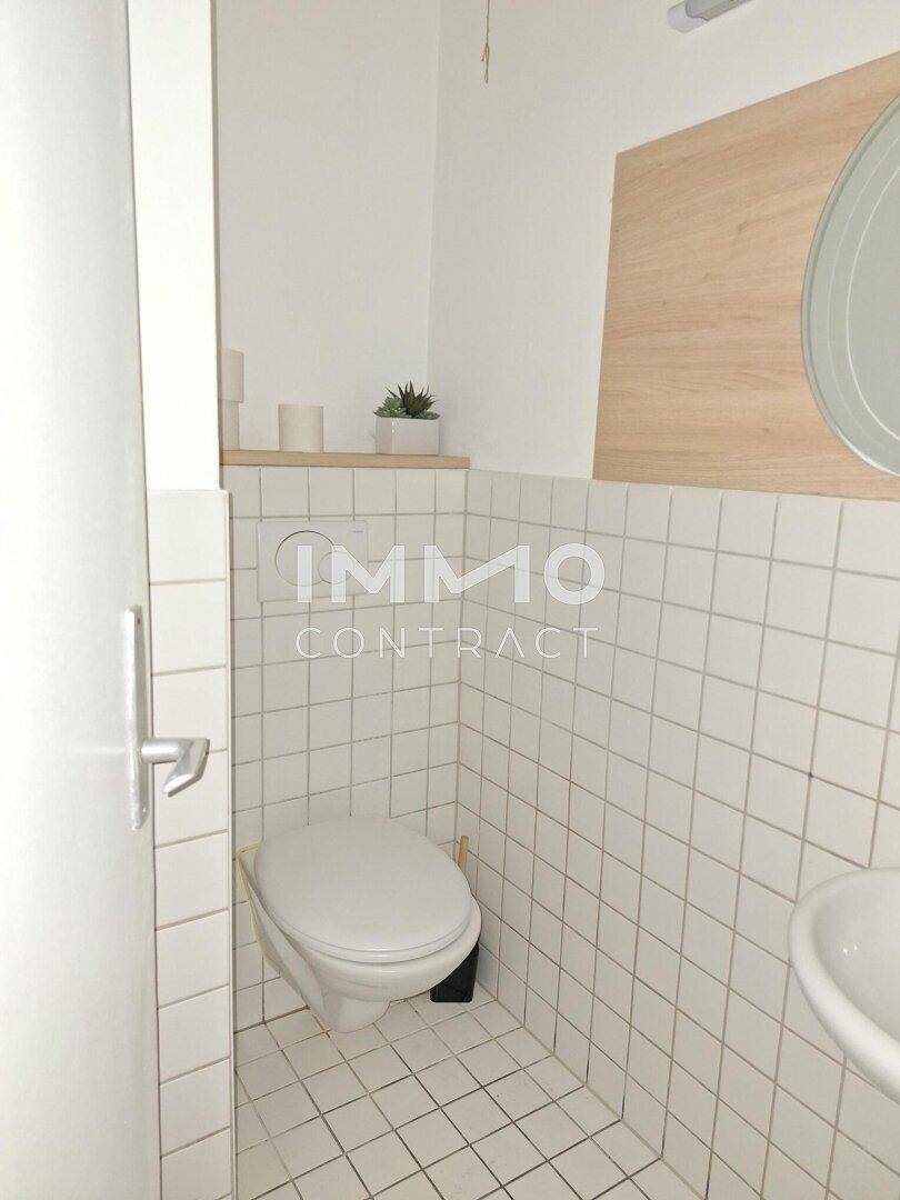 Einfache Toilette mit Wand-WC und kleinem Waschbecken, gefliest mit weißen Quadratfliesen.