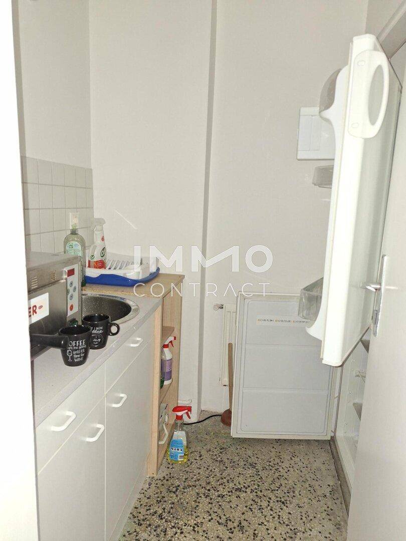 Kleine Küchenzeile mit Spüle, Kühlschrank und einfacher Ausstattung in einem schmalen Raum.