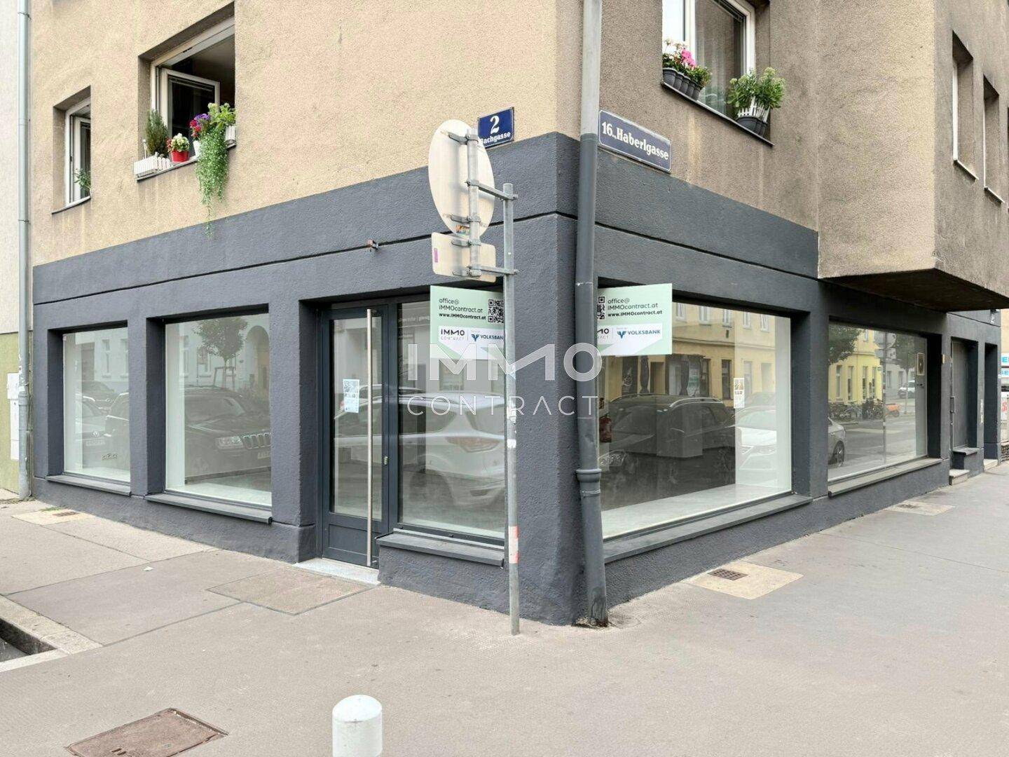 Eckgebäude mit großen Schaufenstern und dunkler Fassade an einer städtischen Straße.