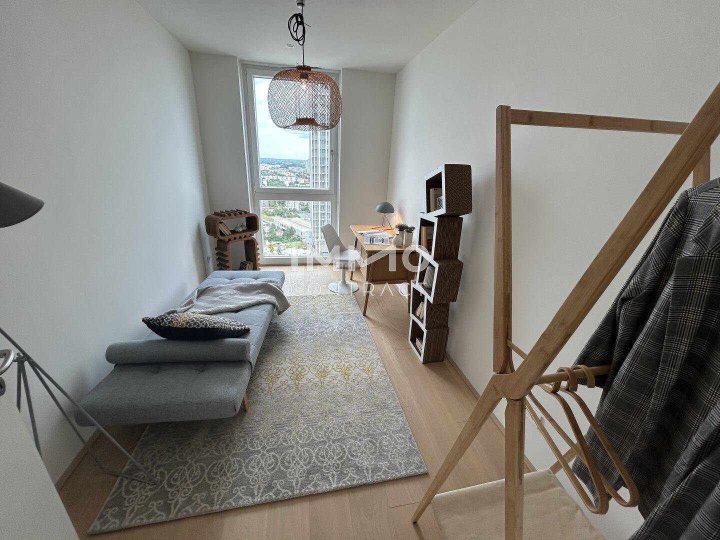 Funktionales Arbeitszimmer mit Holzboden, Tagesbett und großem Fenster, das viel natürliches Licht hereinlässt.