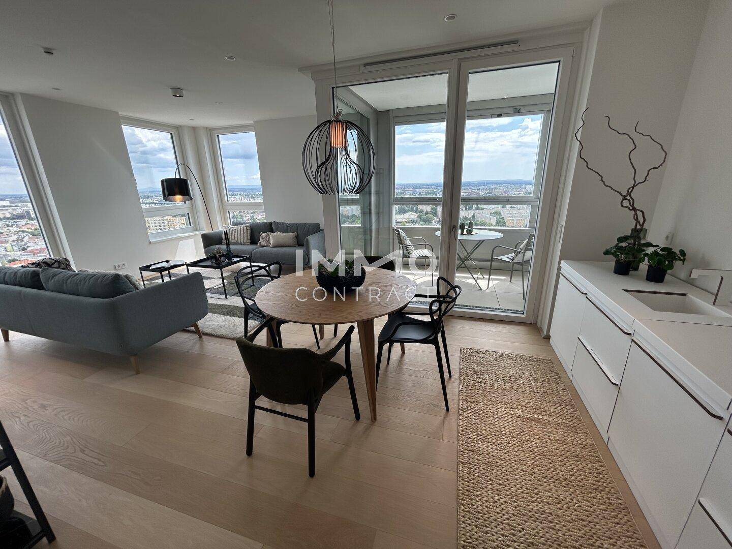 Moderner Wohn-Essbereich mit Holzboden, stilvollen Möbeln und direktem Zugang zum verglasten Balkon mit Aussicht.