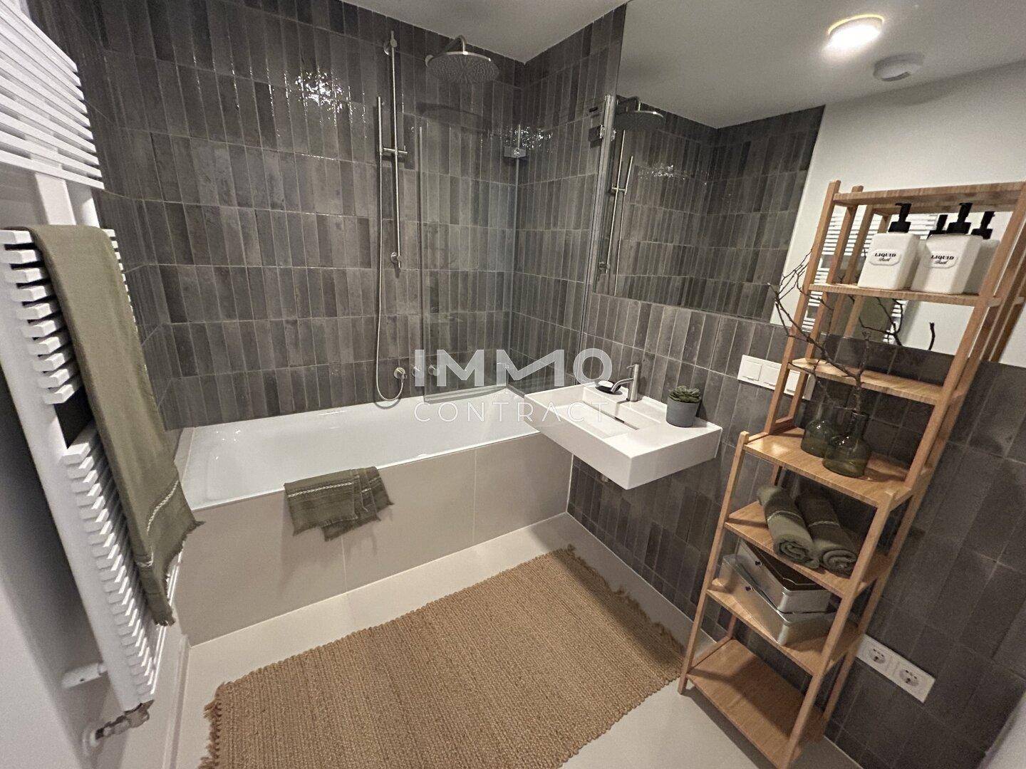 Modernes Badezimmer mit dunklen Fliesen, Badewanne, Regendusche und beheiztem Handtuchhalter.