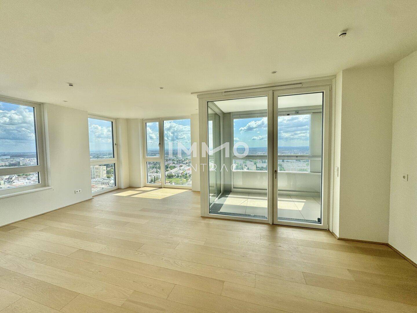 Geräumiges, helles Wohnzimmer mit großen Fenstern, Holzboden und Zugang zu einem verglasten Balkon mit Panoramablick.