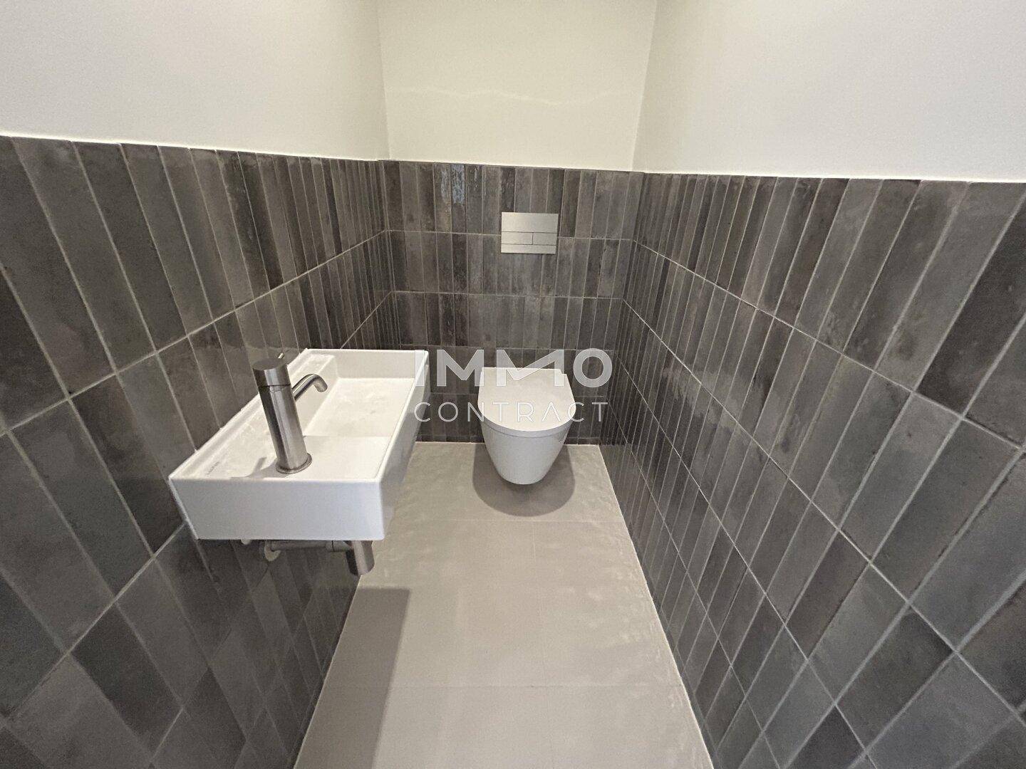 Modernes Gäste-WC mit dunklen Fliesen, wandmontierter Toilette und einem stilvollen Waschbecken.