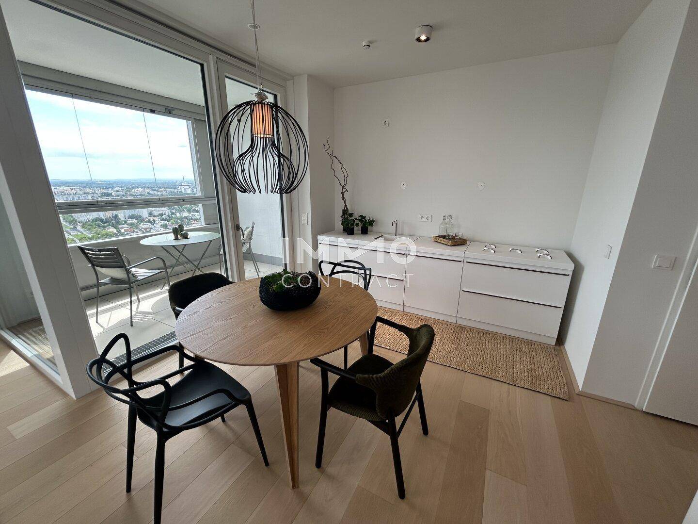 Essbereich mit Holztisch, modernen Stühlen und einer Küchenzeile, direkt am verglasten Balkon mit Weitblick.