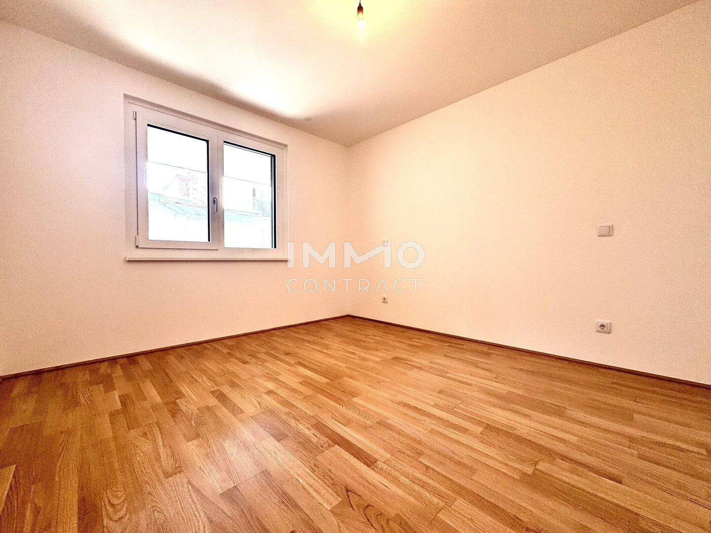 Helles Schlafzimmer mit Parkettboden und einem Fenster, bereit zur individuellen Gestaltung.
