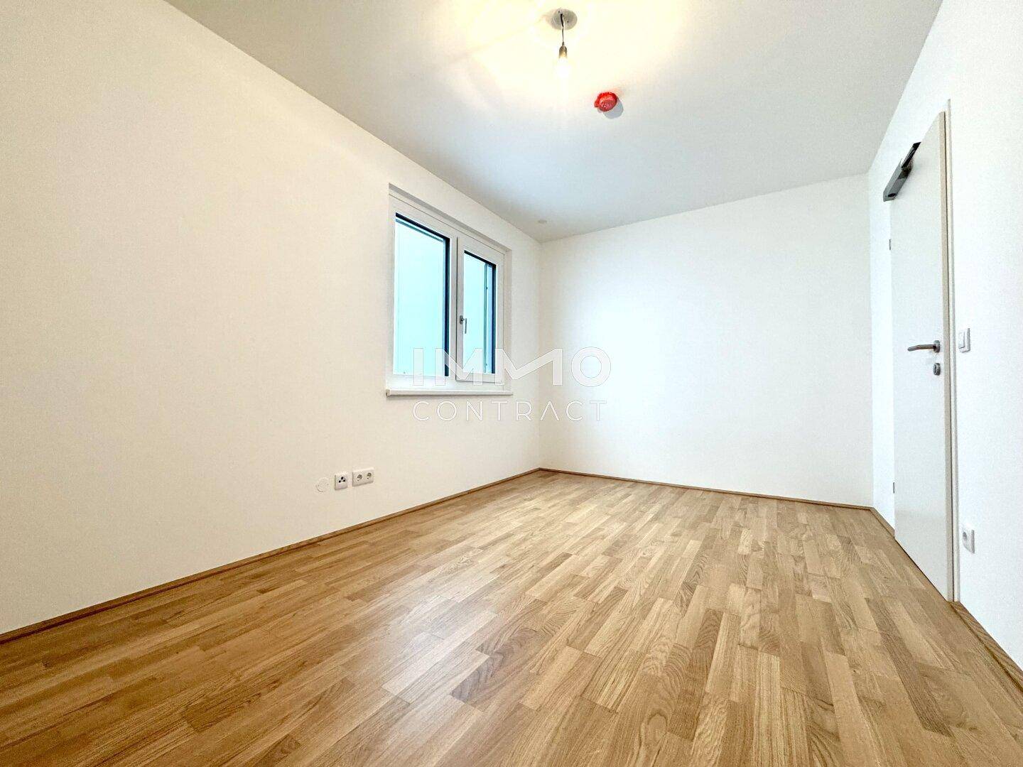 Helles Zimmer mit Parkettboden und einem Fenster, ideal als Schlaf- oder Arbeitszimmer.