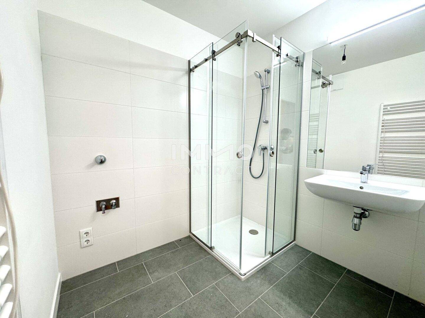 Modernes Badezimmer mit Duschkabine, Waschbecken und beheiztem Handtuchhalter.