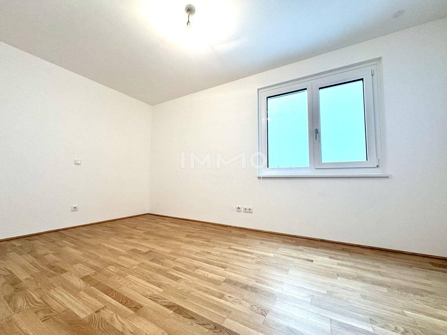 Freundliches Zimmer mit Holzparkett und großem Fenster für viel Tageslicht.