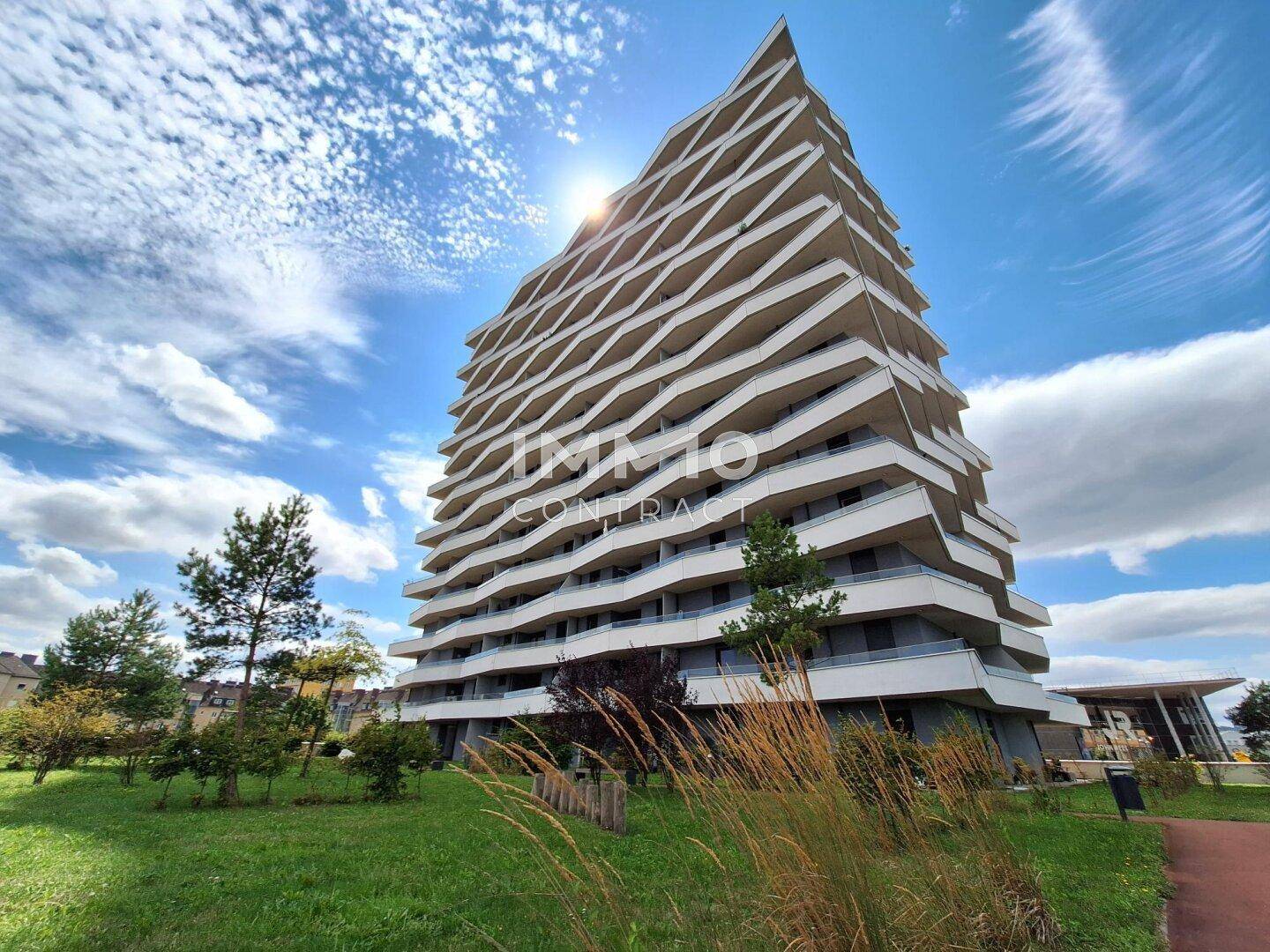 Modernes Wohngebäude mit markanter Architektur, umgeben von Grünflächen unter sonnigem Himmel.