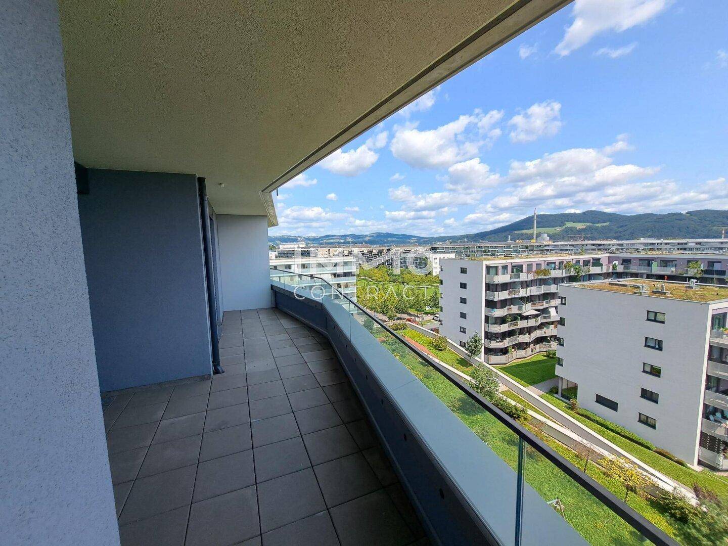 Langer Balkon mit Glasgeländer und weitem Blick über die Stadt und umliegende Gebäude.