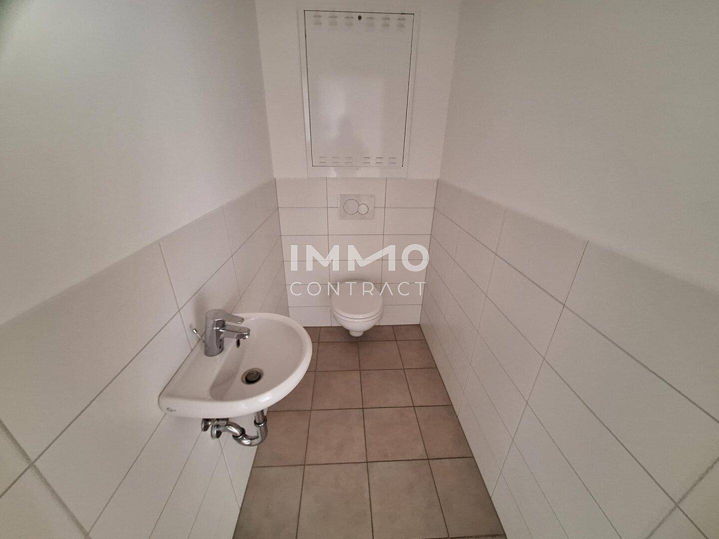 Gäste-WC mit Wand-WC, kleinem Waschbecken und weißen Fliesen an den Wänden.