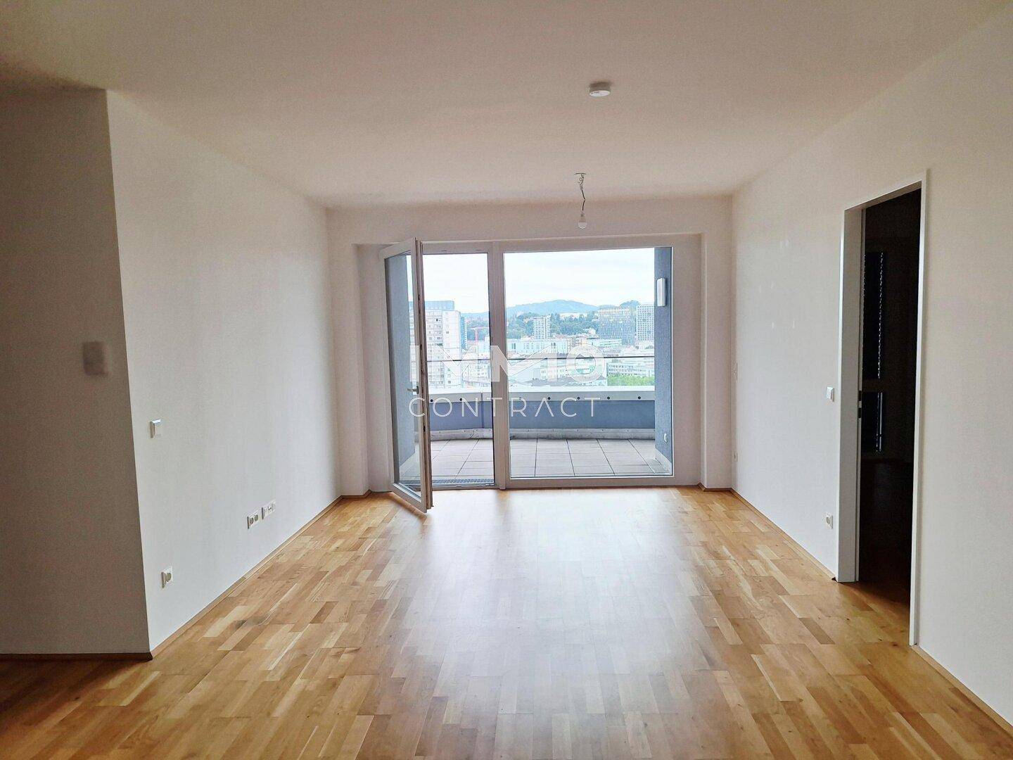 Geräumiges Wohnzimmer mit Parkettboden und Zugang zu einem großen Balkon.