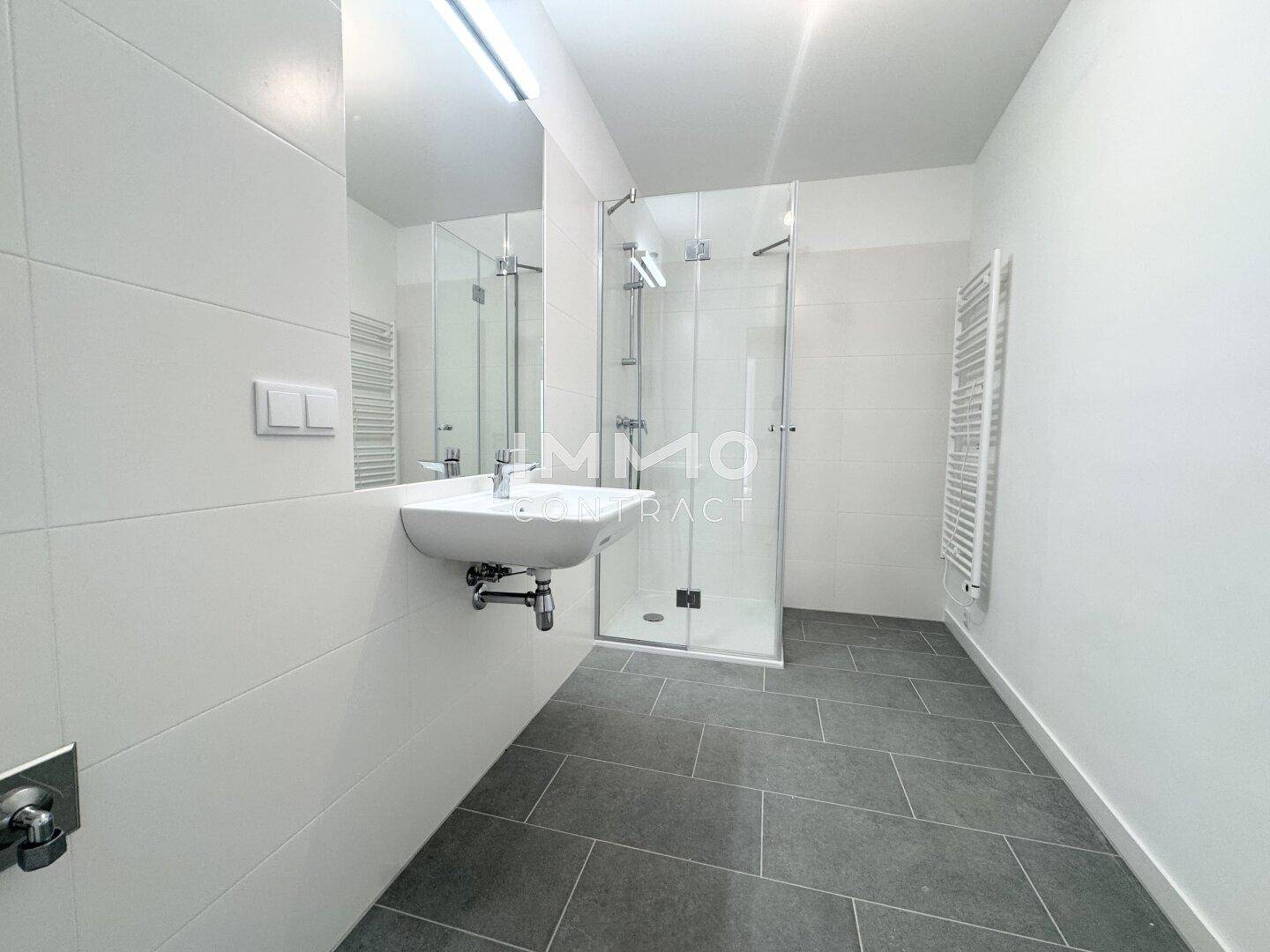 Modernes Badezimmer mit großer Duschkabine, weißen Fliesen und beheiztem Handtuchhalter.