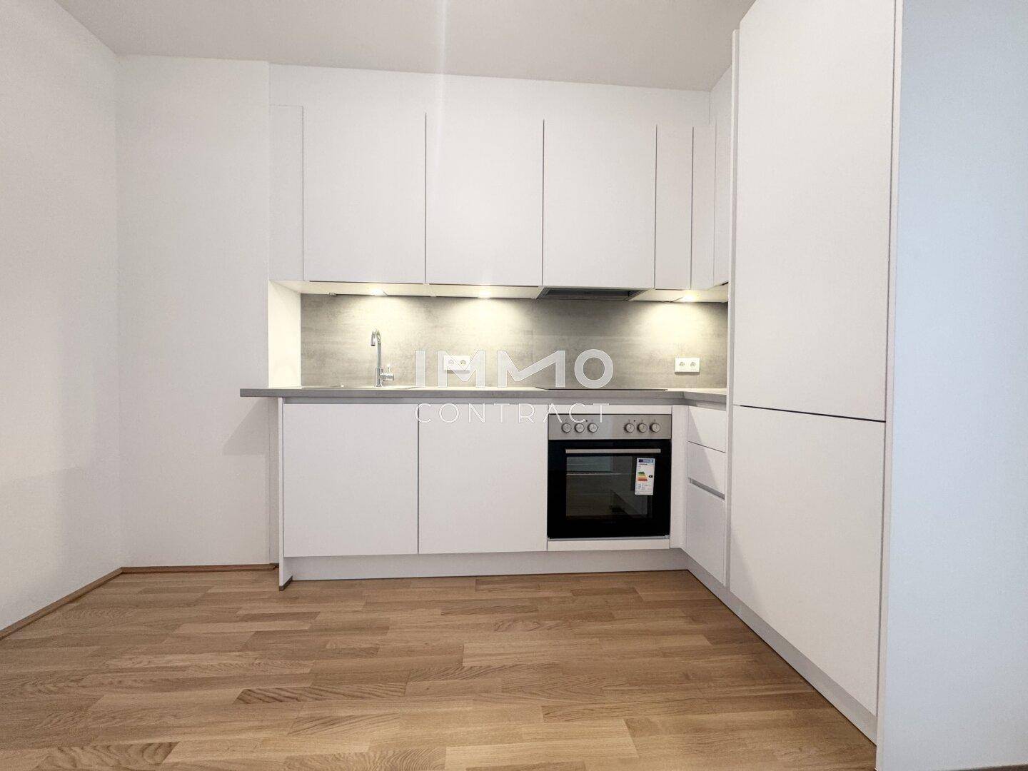 Moderne Einbauküche in Weiß mit integriertem Backofen und hellem Holzparkettboden.