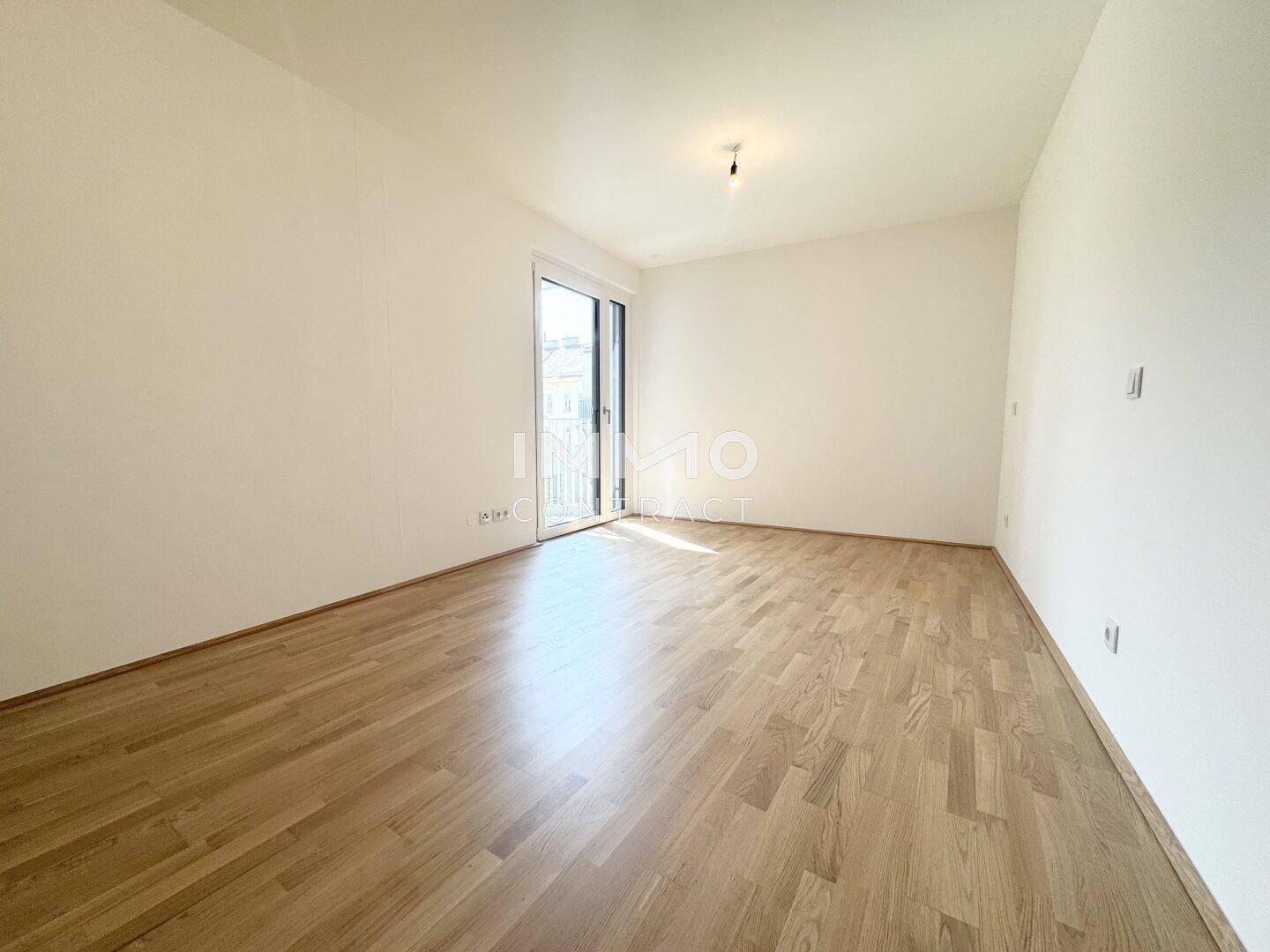 Lichtdurchflutetes Zimmer mit Parkettboden und Zugang zu einem privaten Balkon.