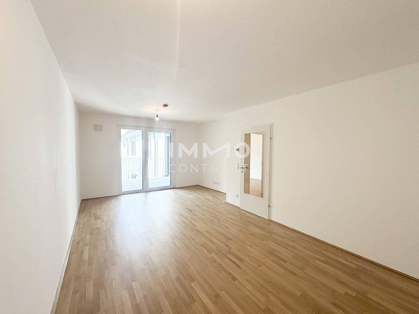 Geräumiges, helles Zimmer mit Parkettboden und großen Fenstern, ideal als Wohnbereich.