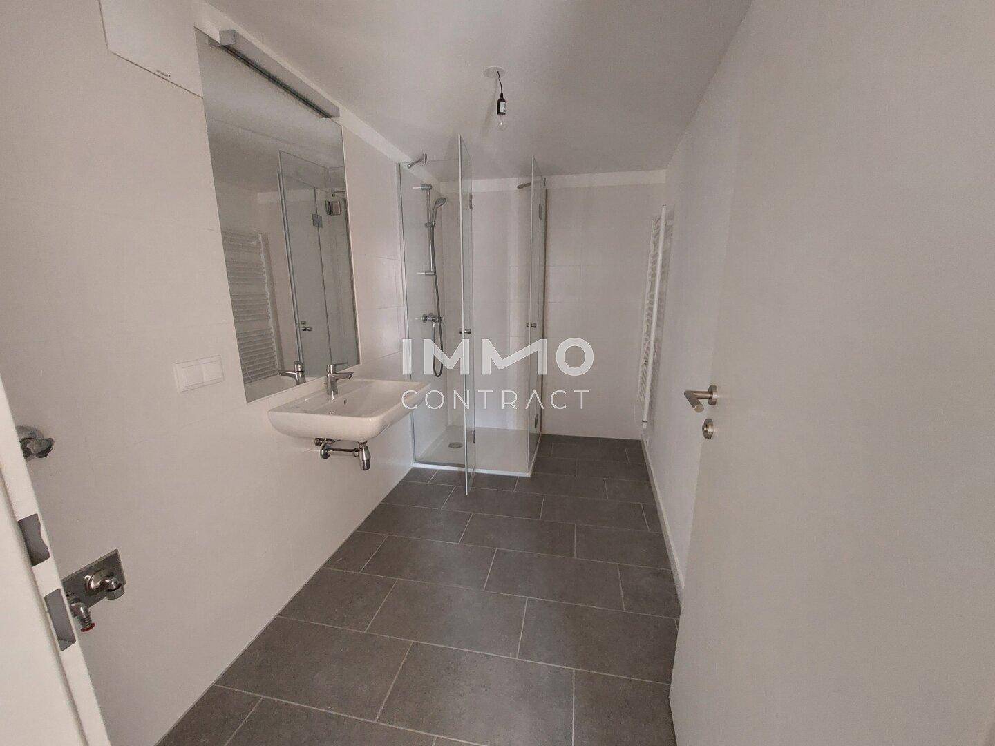 Modernes Badezimmer mit Dusche, Einzelwaschbecken und grauem Fliesenboden.