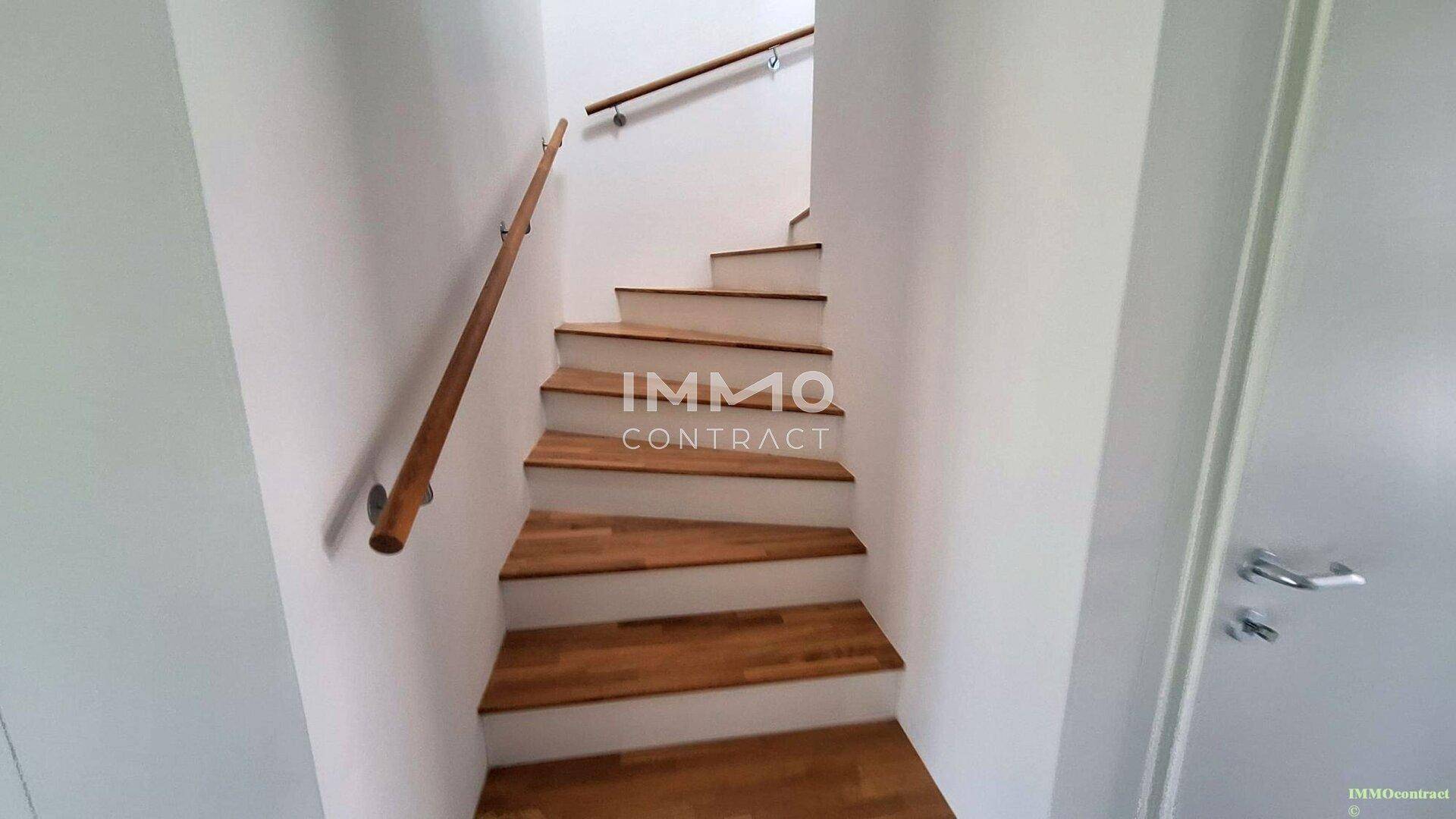 Moderne Holztreppe mit weißem Geländer, die die verschiedenen Etagen verbindet.