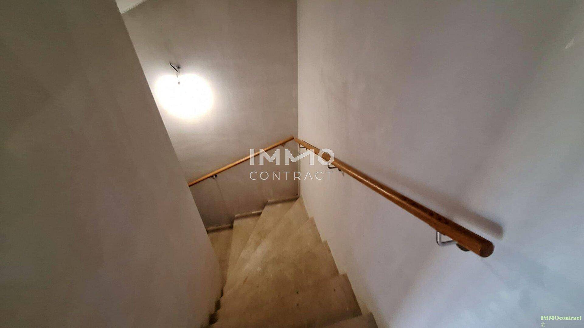 Treppenhaus mit Holzgeländer und weiß gestrichenen Wänden, das nach oben führt.