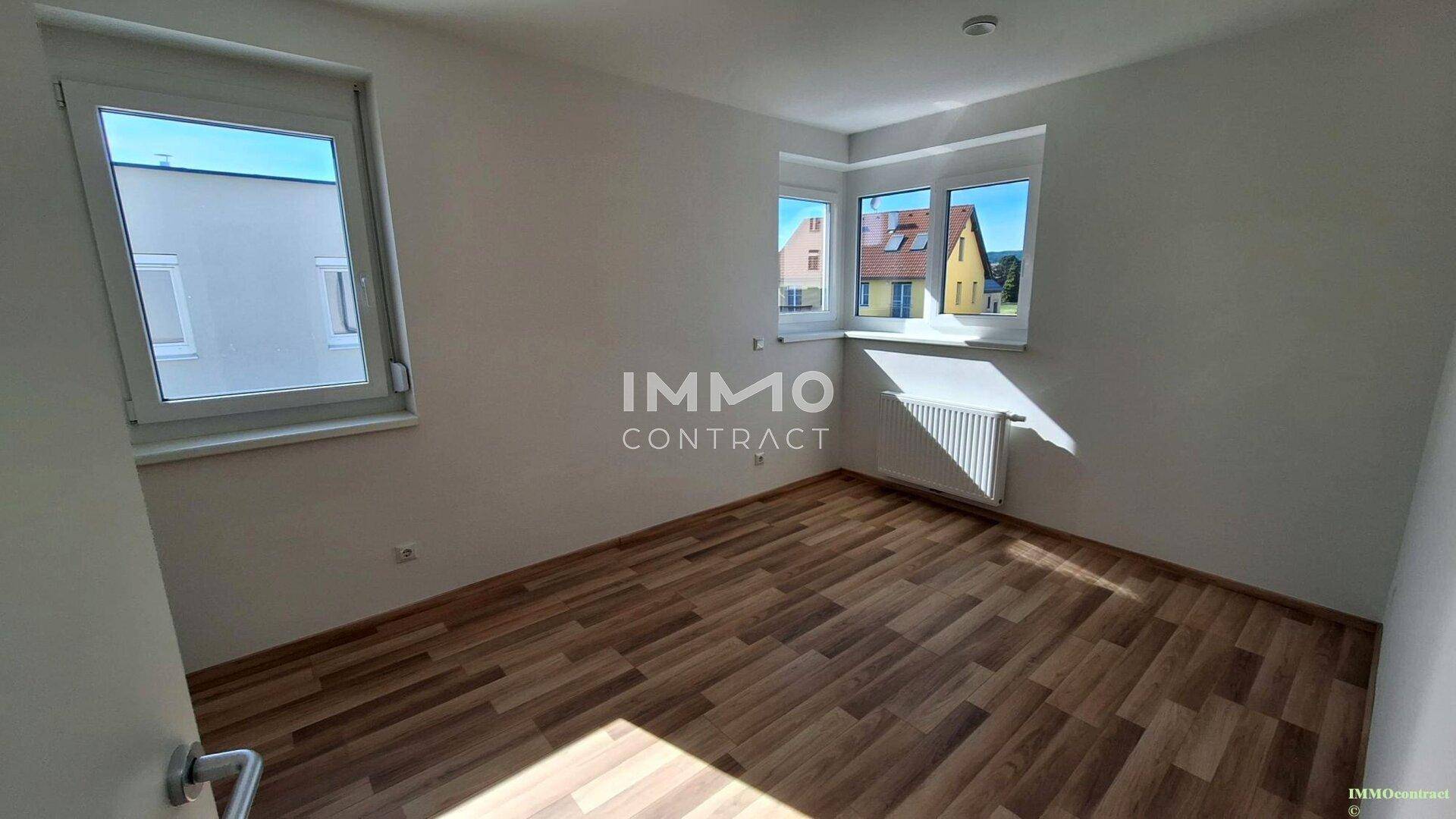 Helles Schlafzimmer mit Laminatboden und Fenstern mit Blick ins Grüne.