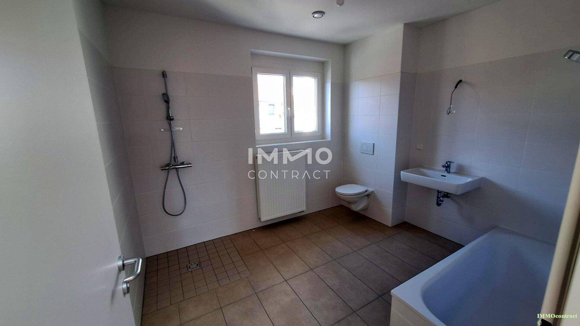 Modernes Badezimmer mit Badewanne, Dusche, WC und Fenster, komplett gefliest.