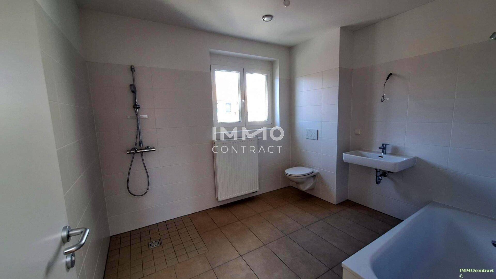 Modernes Badezimmer mit Badewanne, Dusche, WC und Fenster, komplett gefliest.
