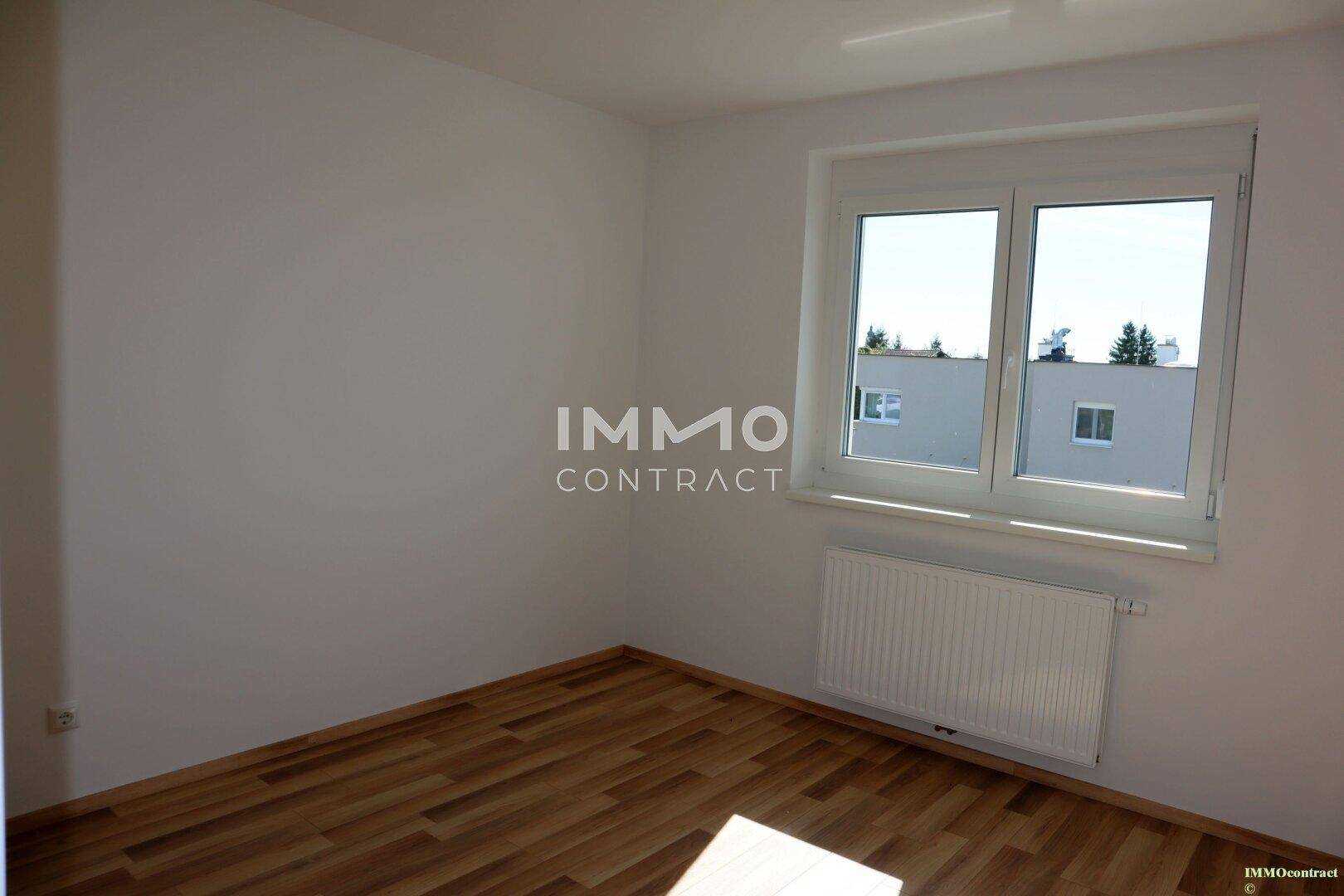 Lichtdurchflutetes Schlafzimmer mit Holzboden und Blick auf die umliegenden Häuser.
