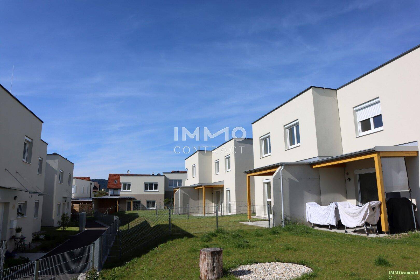 Reihenhaussiedlung mit gepflegten Gärten und Terrassen unter blauem Himmel.
