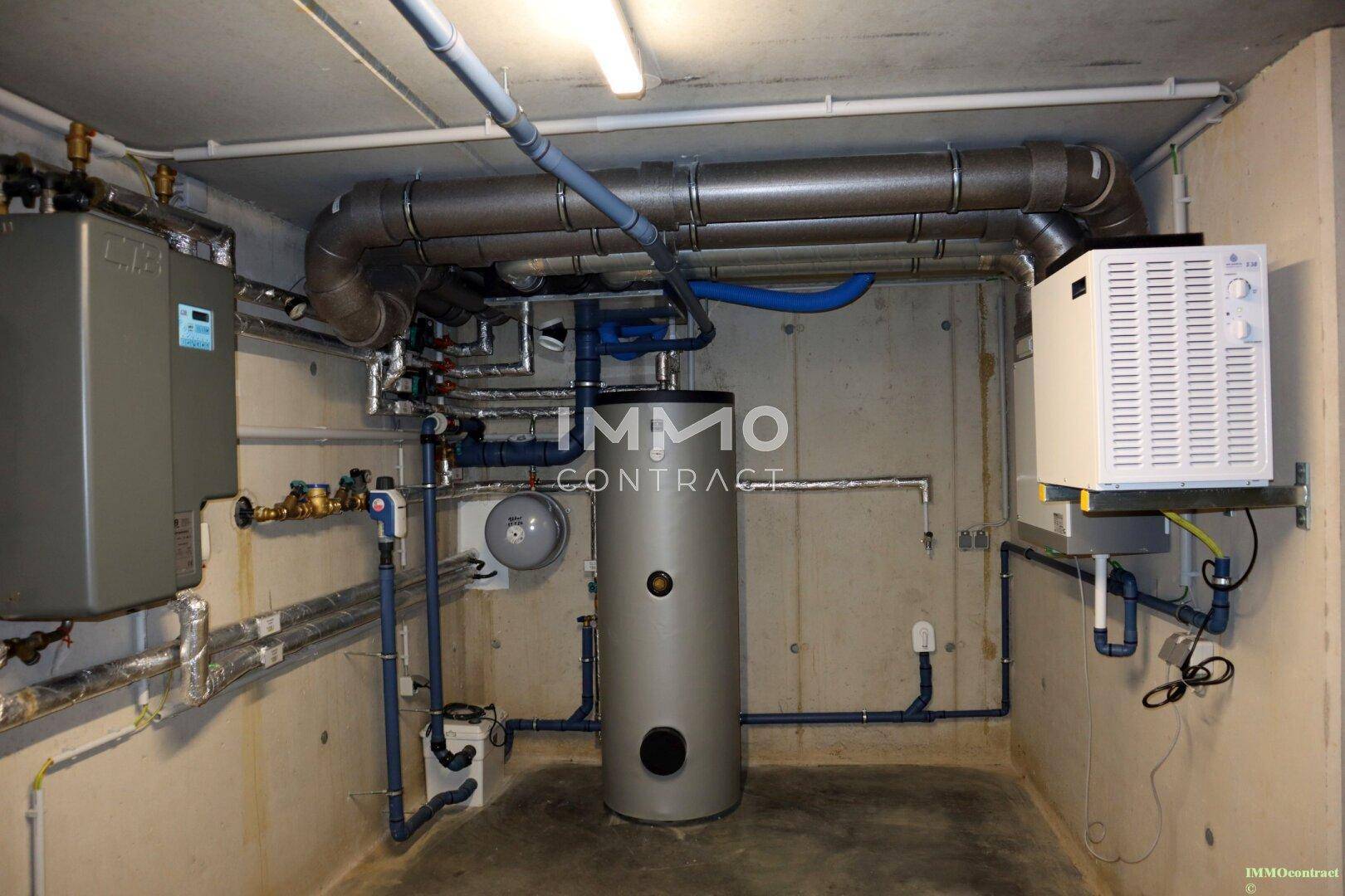 Technikraum im Keller mit Heizungsanlage, Warmwasserspeicher und Rohrleitungen.