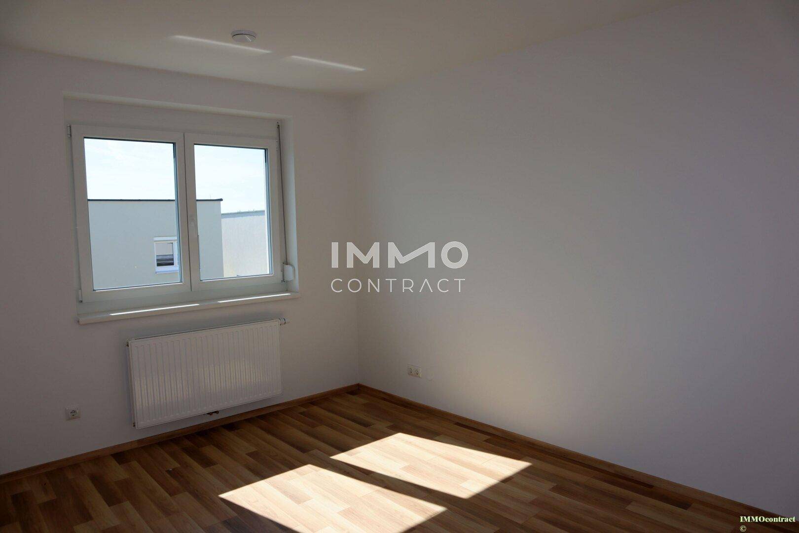 Helles Schlafzimmer mit Parkettboden und Blick auf die umliegenden Häuser.