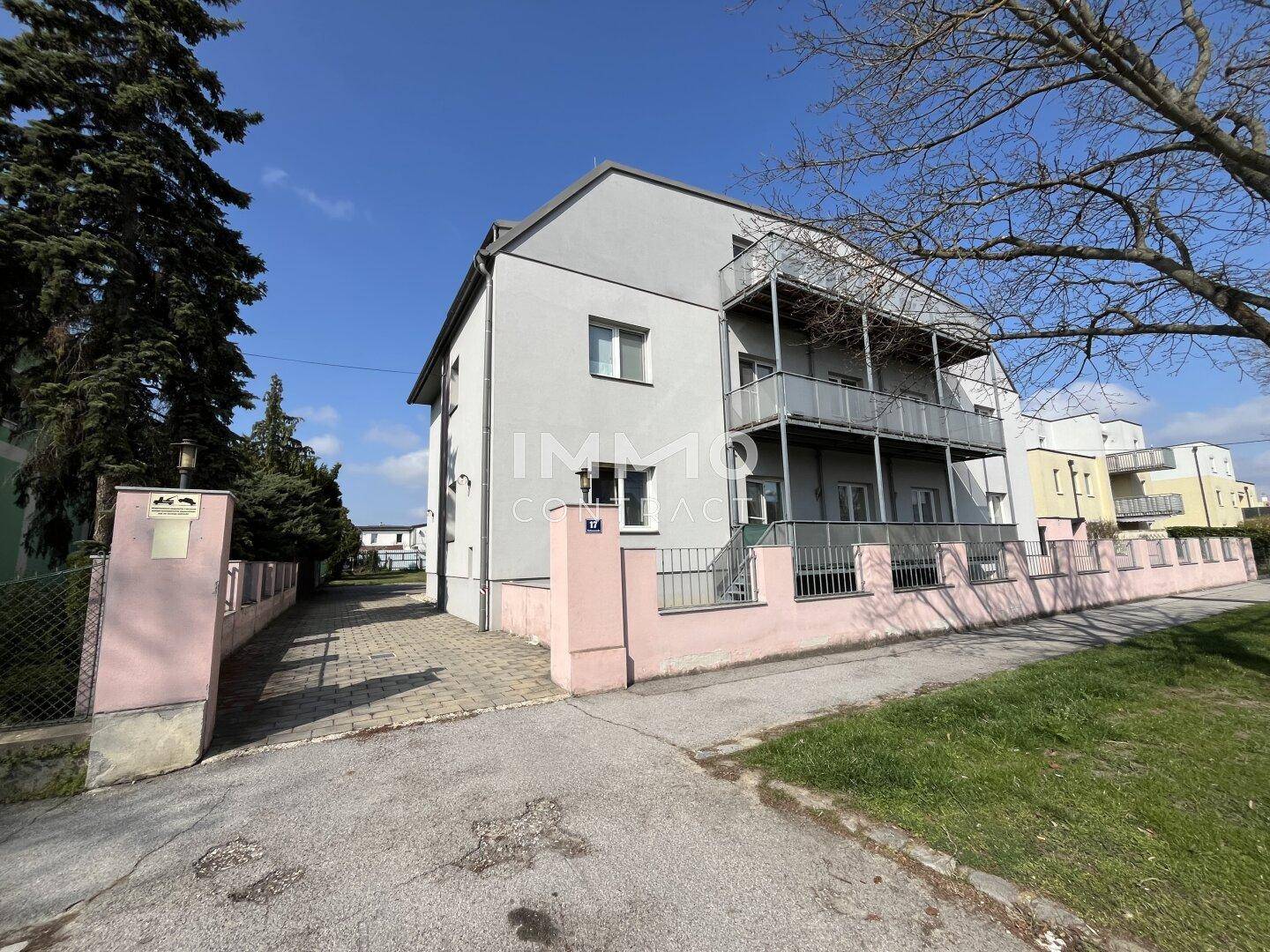 Seitenansicht des Mehrfamilienhauses mit Eingangsbereich, gepflasterter Zufahrt und Balkonen.