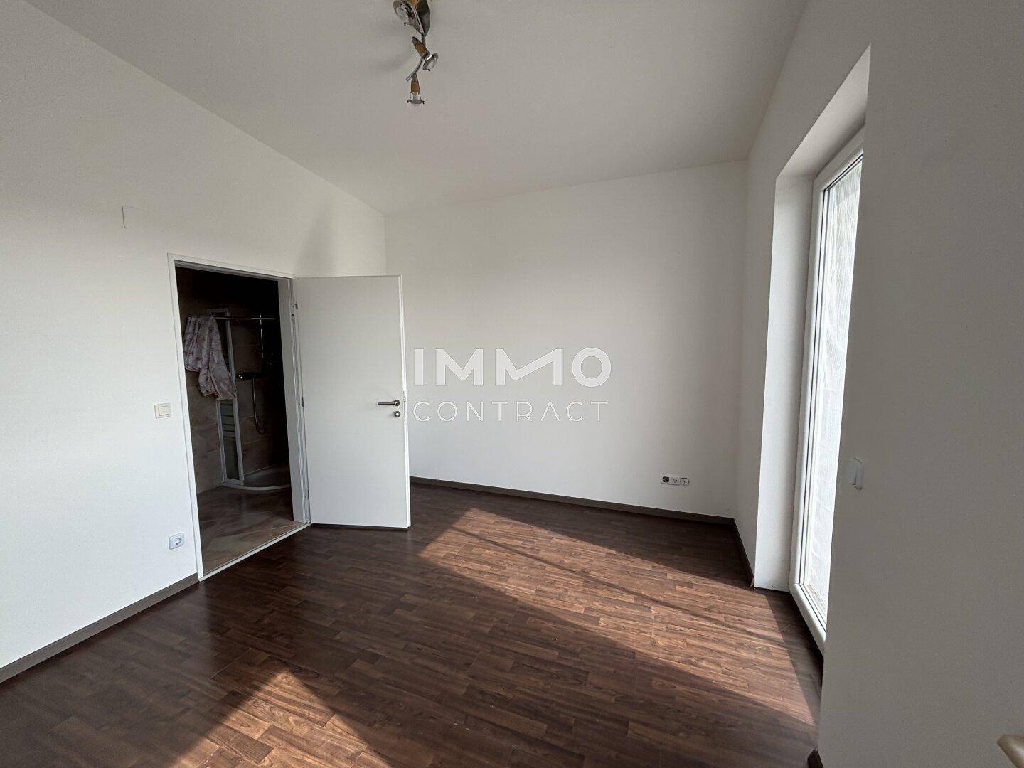 Helles Schlafzimmer mit dunklem Holzboden und Zugang zu einem angrenzenden Badezimmer.